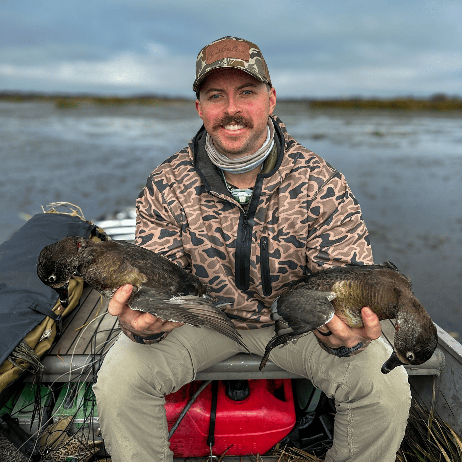 A man is sitting on a boat holding two ducks in his hands.