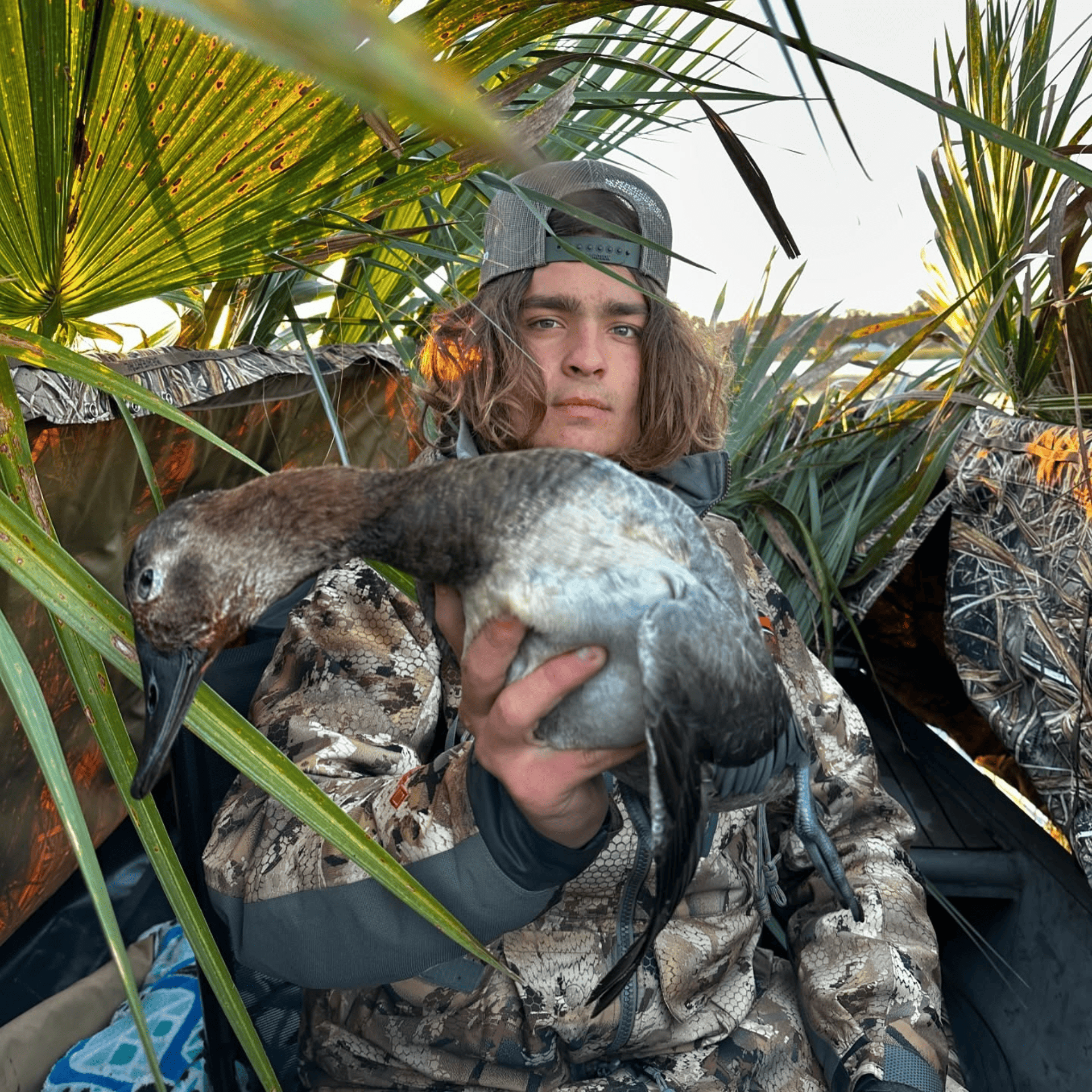 A man in a camouflage jacket is holding a duck in his hands.