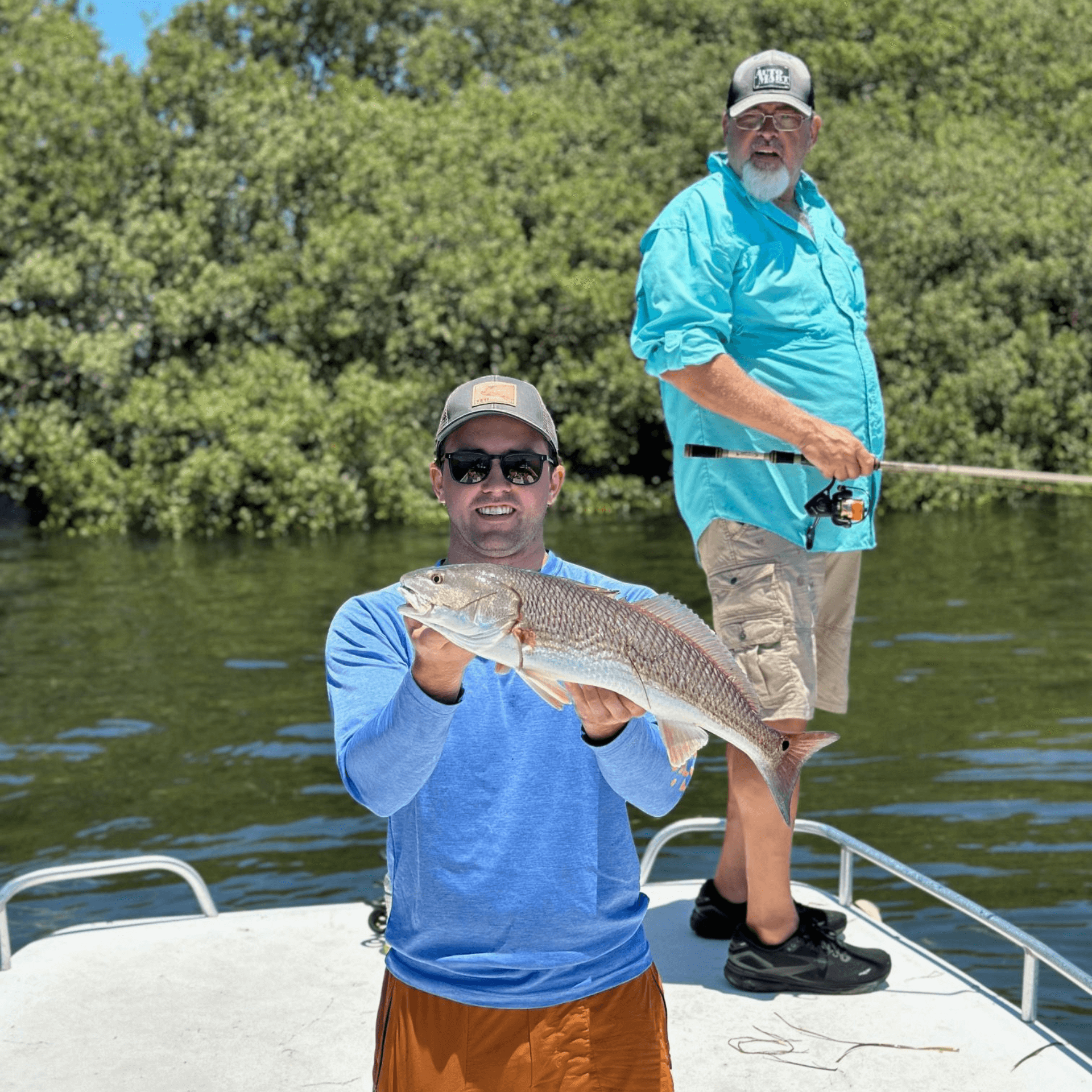 Two men are fishing on a boat and one of them is holding a Redfish.