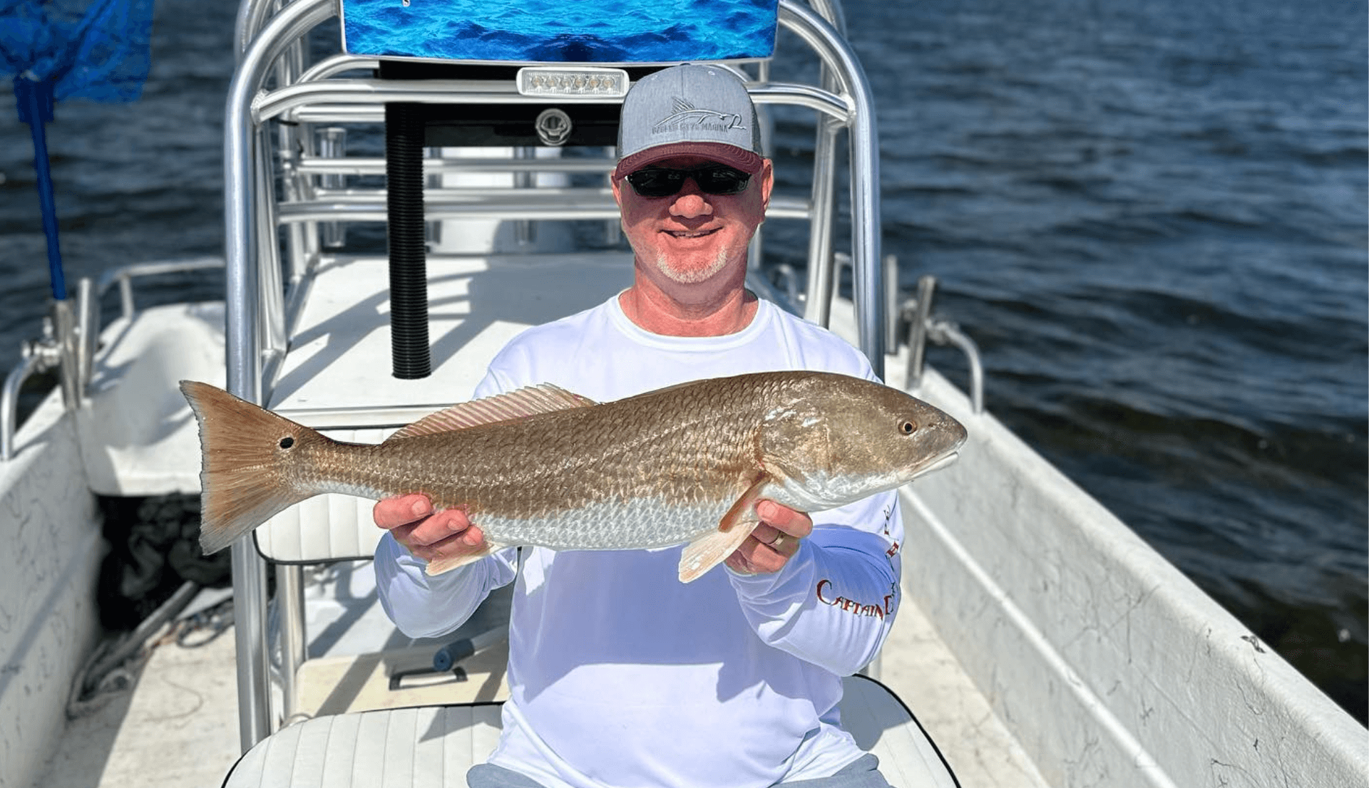 A man is holding a large Redfish on a fishing charter baot.