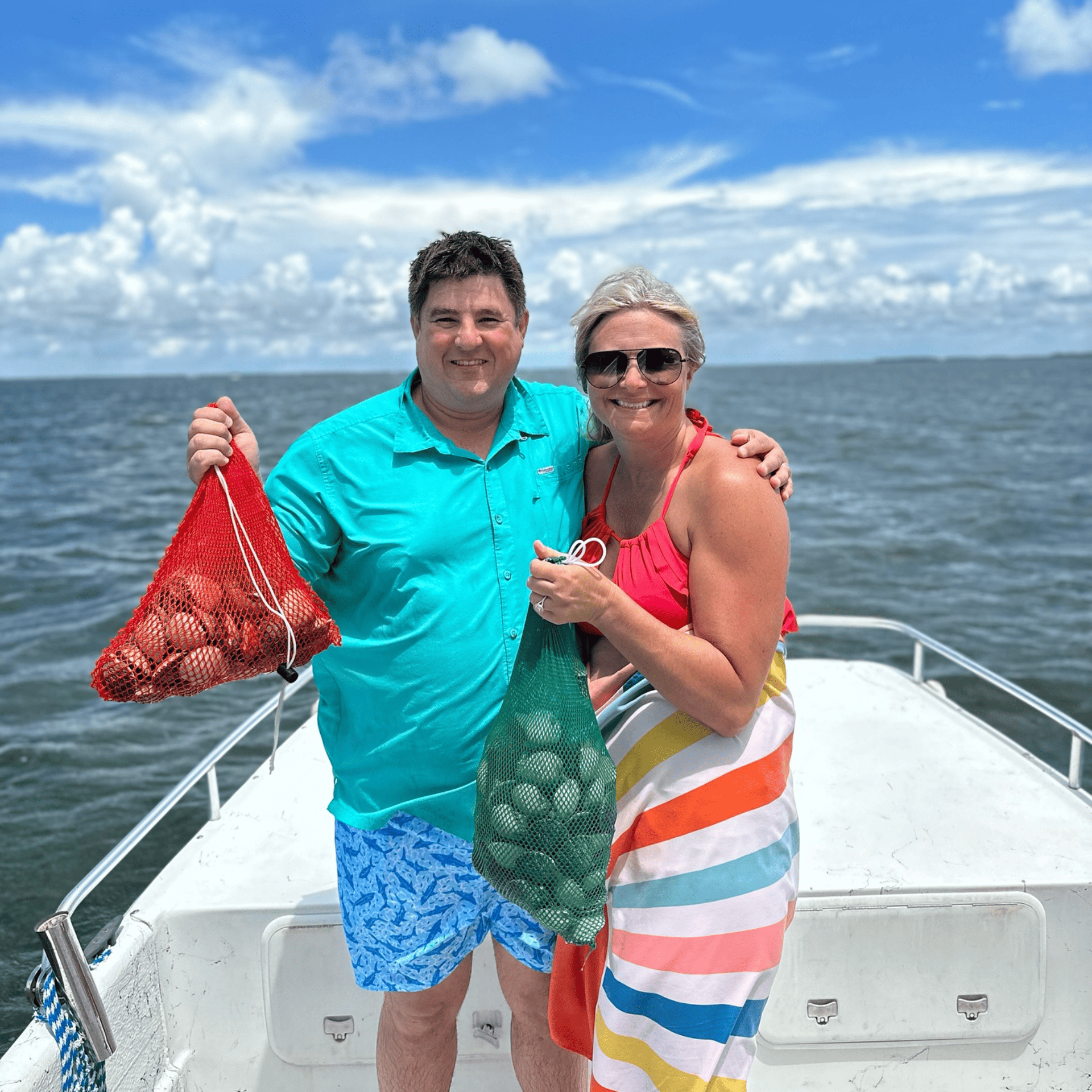 A man and a woman are standing on a boat holding a bag of scallops.