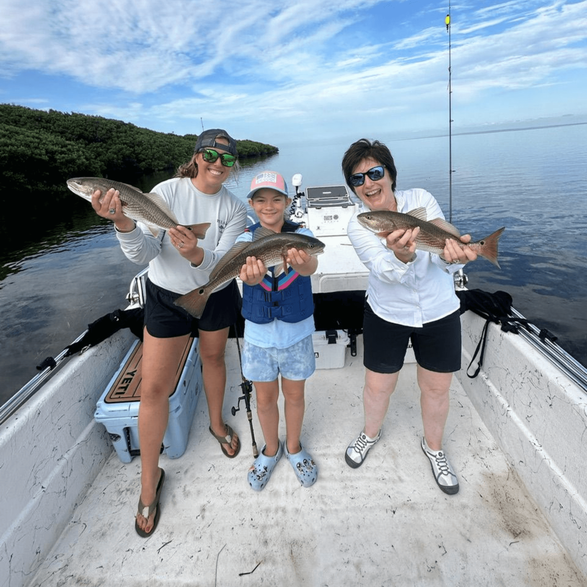 Three people are standing on a boat holding fish in their hands.