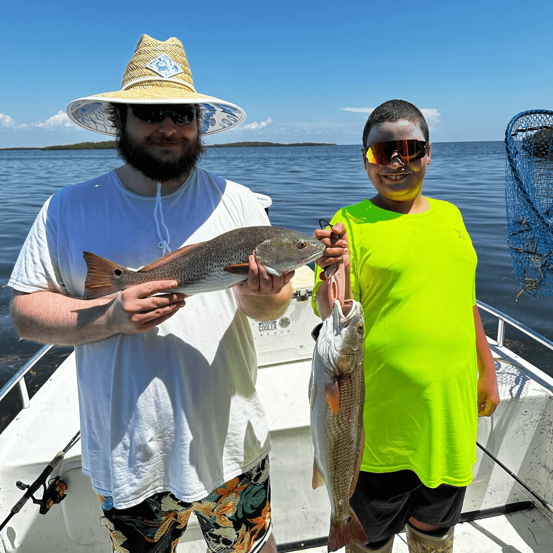 A man and a boy are standing on a boat holding fish.