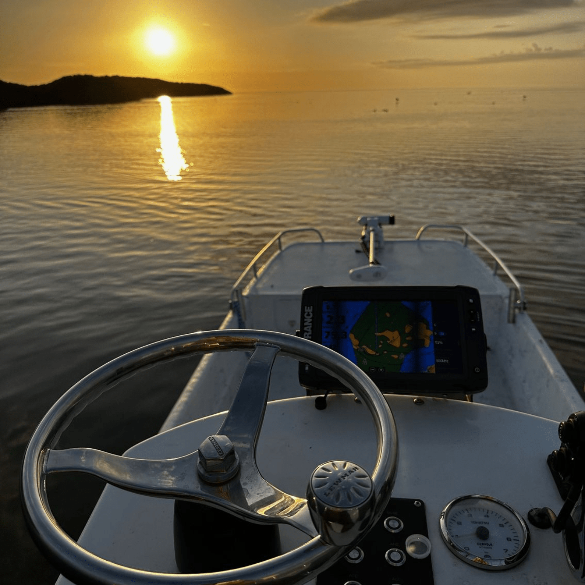 The sun is reflected in the water behind the steering wheel of a boat