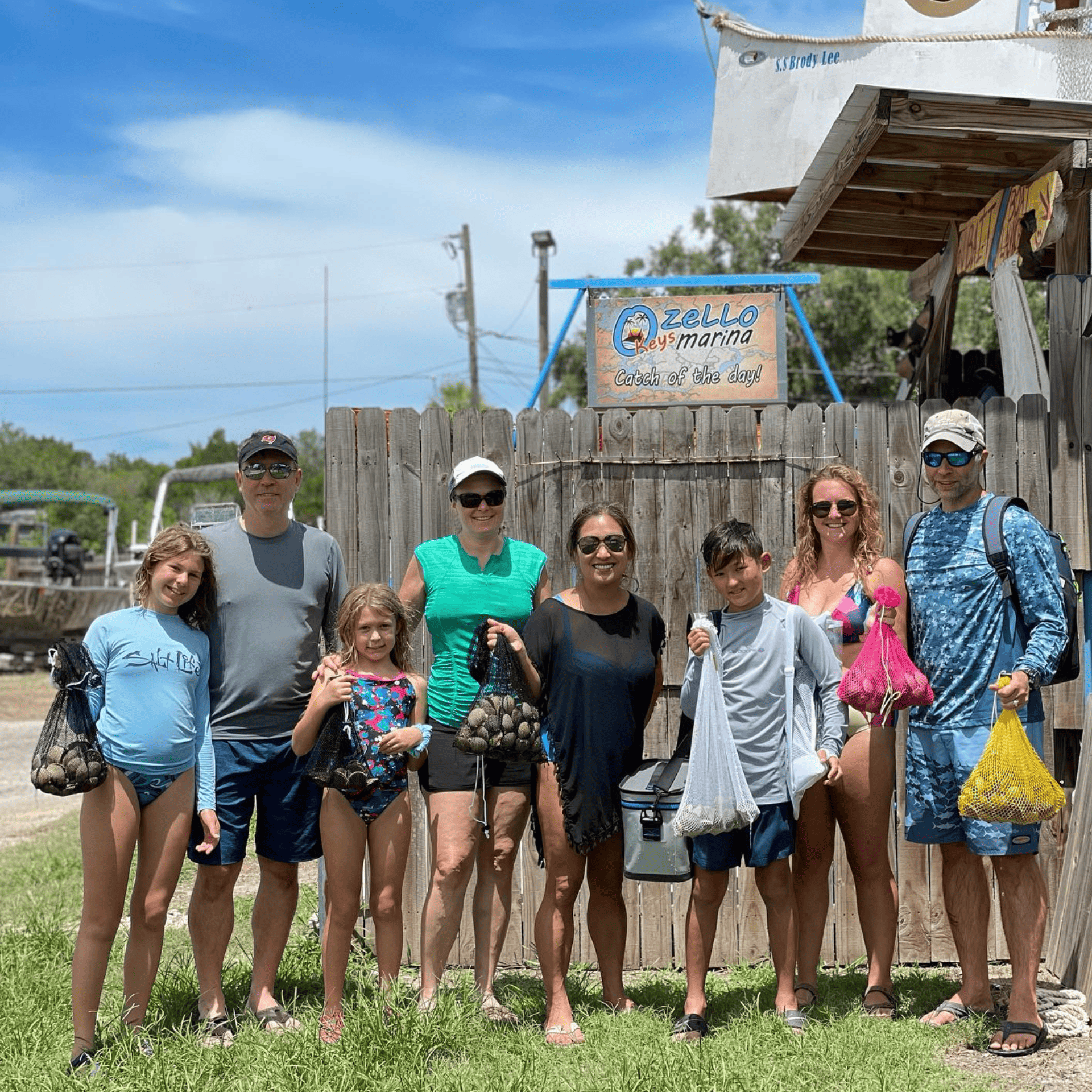 A group of people are posing for a picture in front of a wooden fence holding scallops