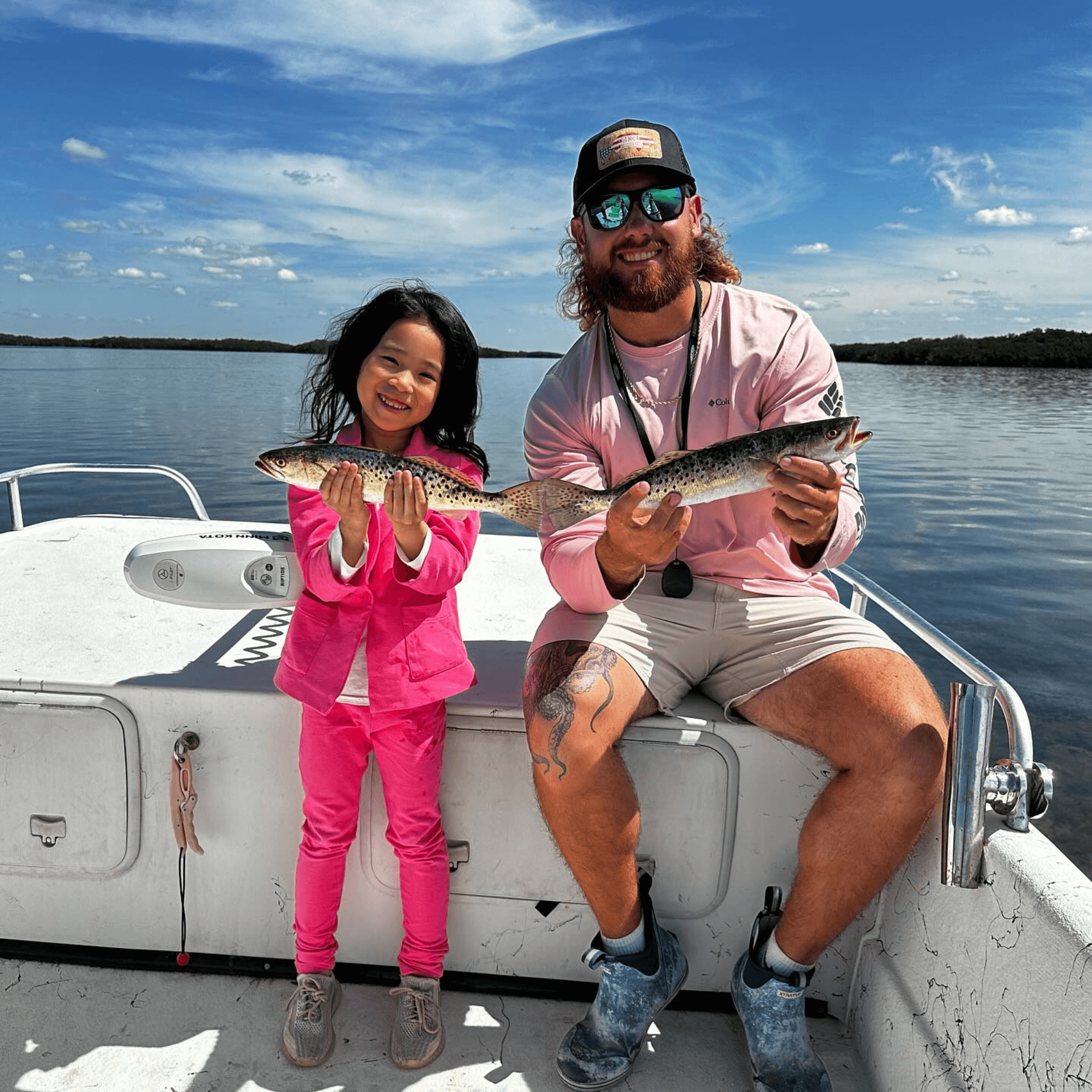 A man and a little girl are sitting on a boat holding fish.