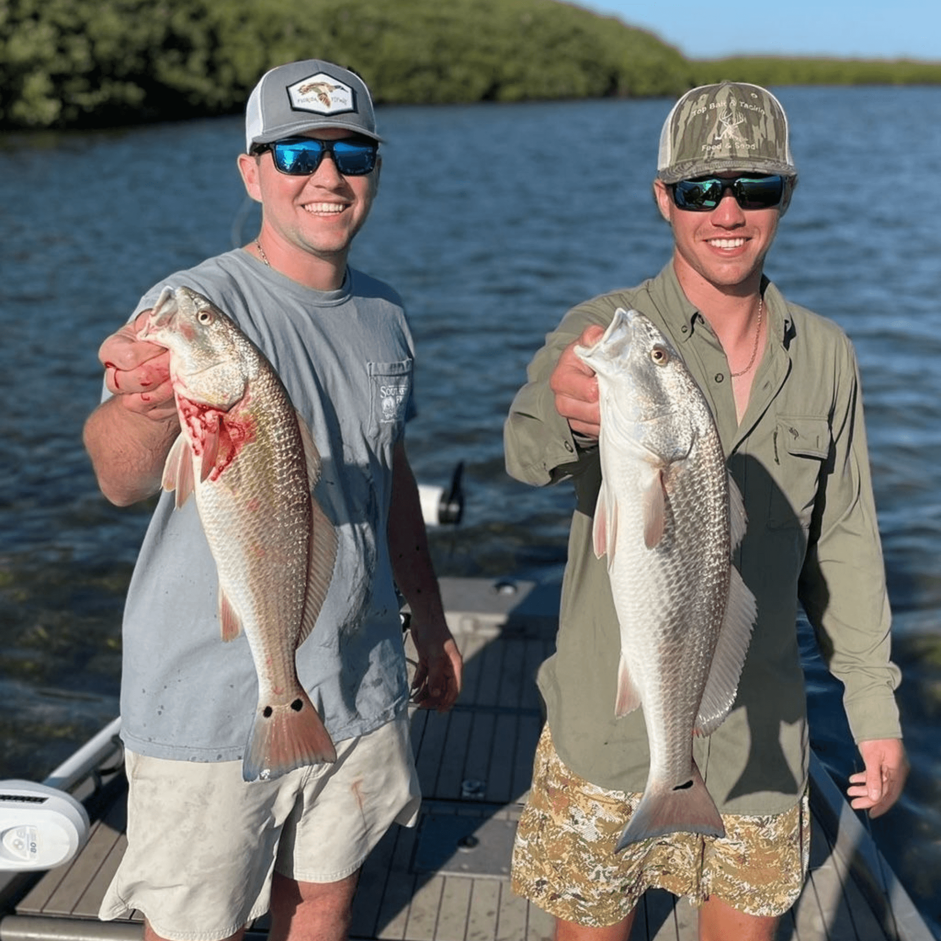 Two men standing on a boat holding Redfish in their hands on a Florida fishing charter.