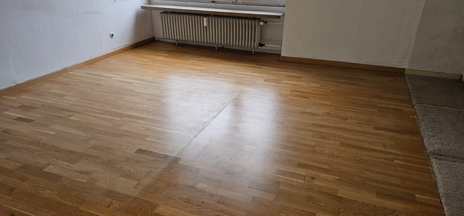 Holzboden in einem leeren Raum mit Heizkörper und Fenster.