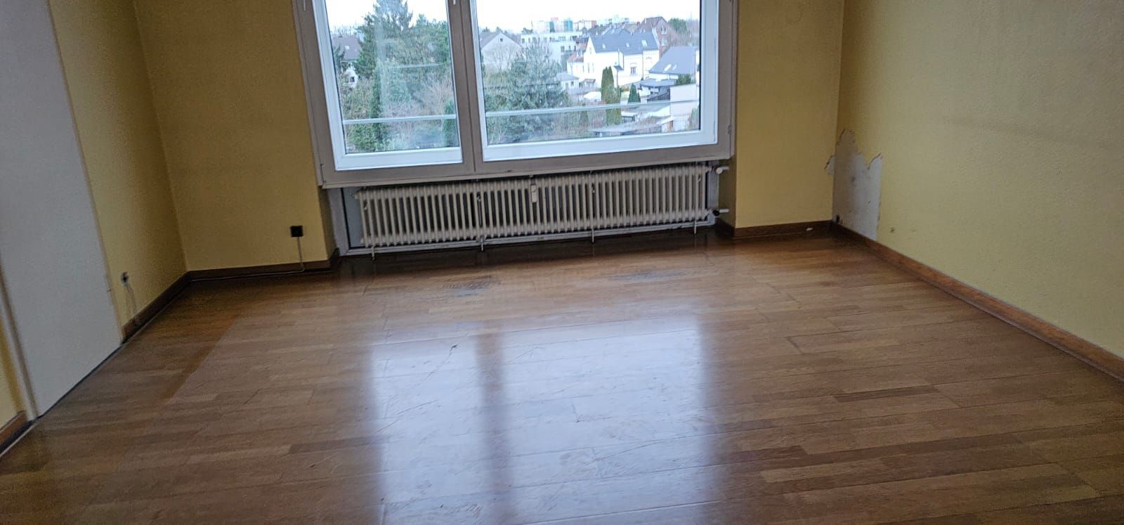 Leerer Raum mit Hartholzböden, einem großen Fenster und einem Heizkörper. Gelbe Wände.