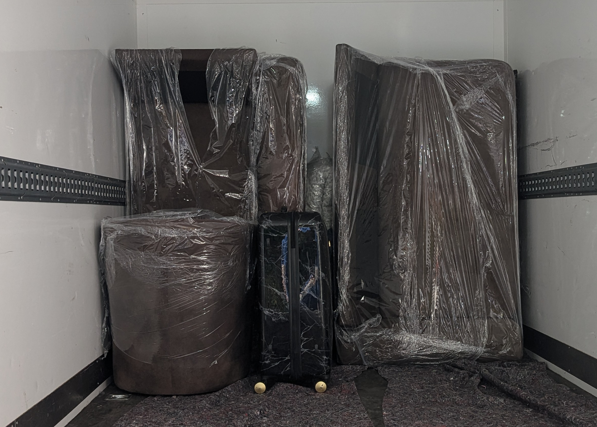 In Plastik eingewickelte Möbel in einem LKW. Enthält einen großen Ottomanen, Stuhllehnen und einen Koffer.