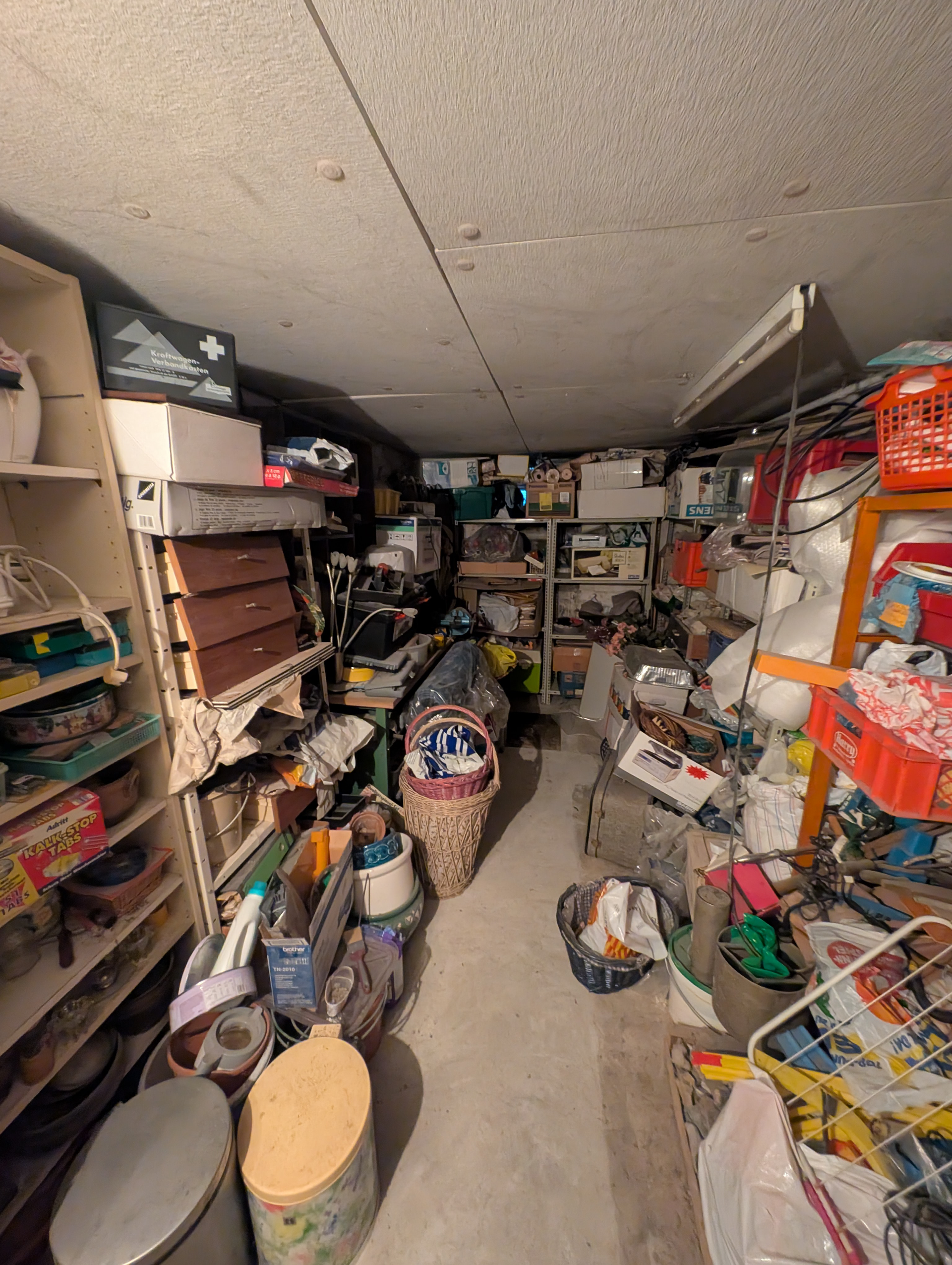 Überfüllter Lagerraum mit überquellenden Regalen und Gegenständen; Kisten, Körbe und verschiedene andere Gegenstände sind gestapelt.