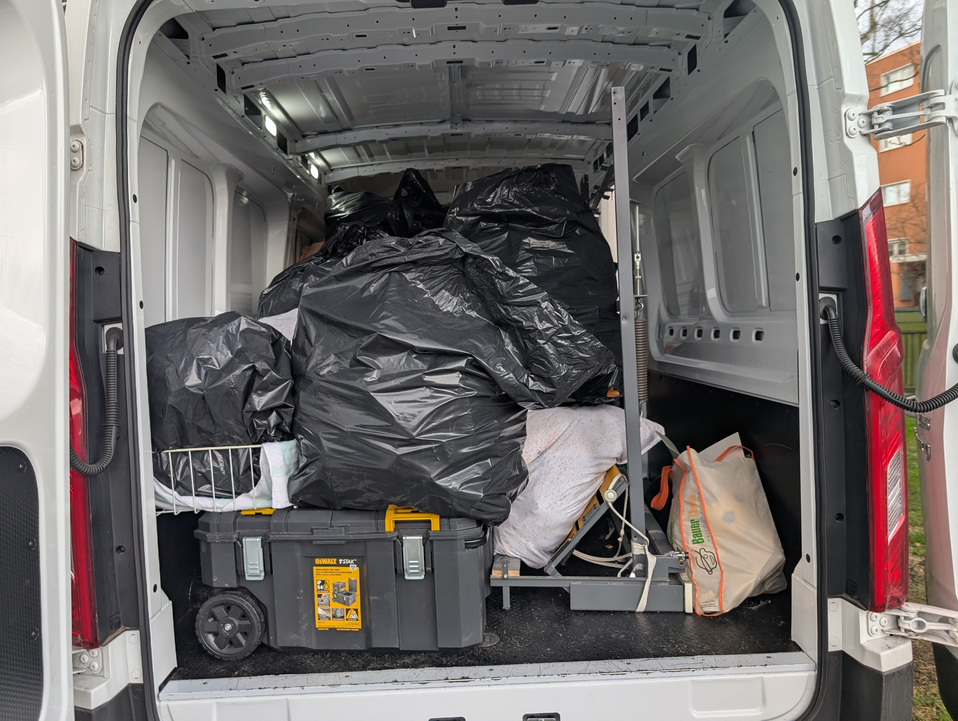 Im Inneren eines weißen Lieferwagens, gefüllt mit schwarzen Müllsäcken, einem Werkzeugkasten und einer Hebebühne.