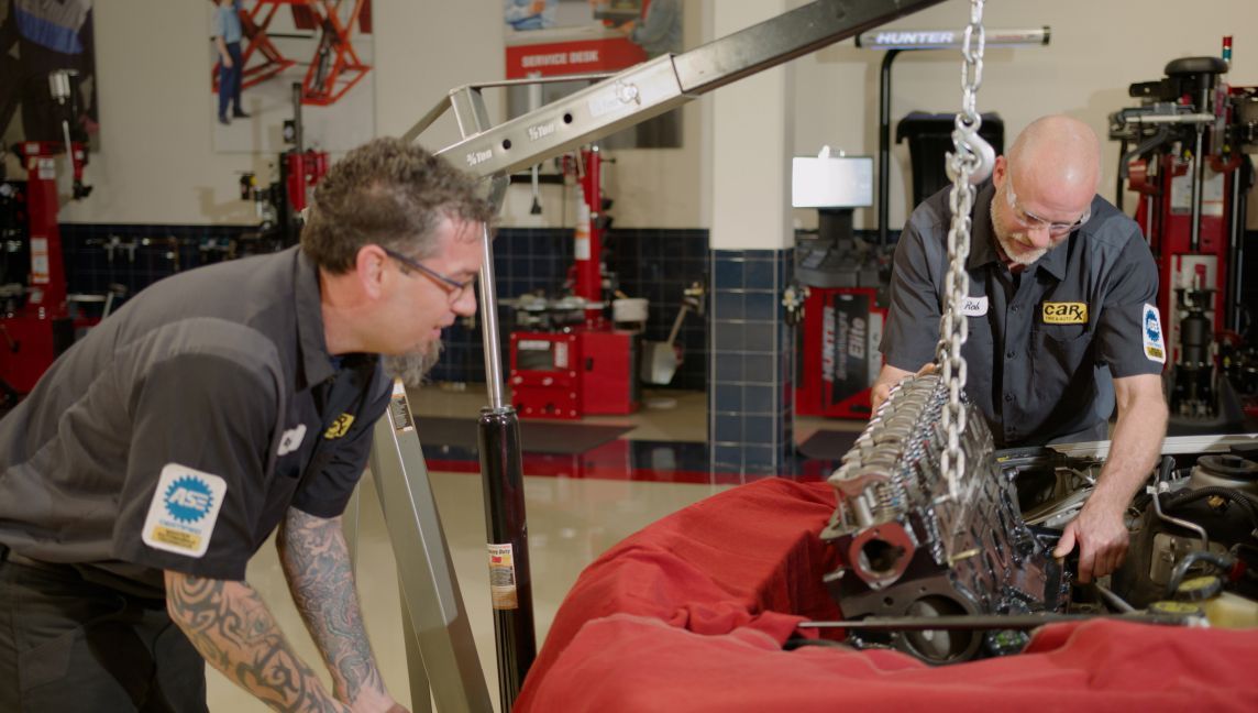 Two mechanics lifting an engine from a car in a garage.
