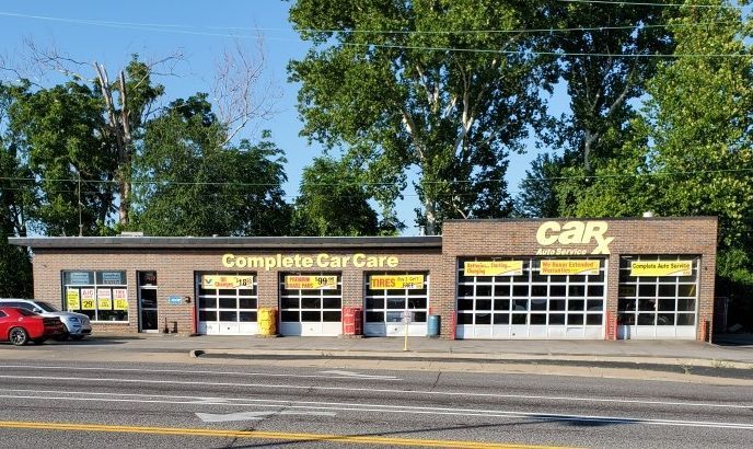 CarX auto repair shop, brick building with garage bays and red car parked out front.