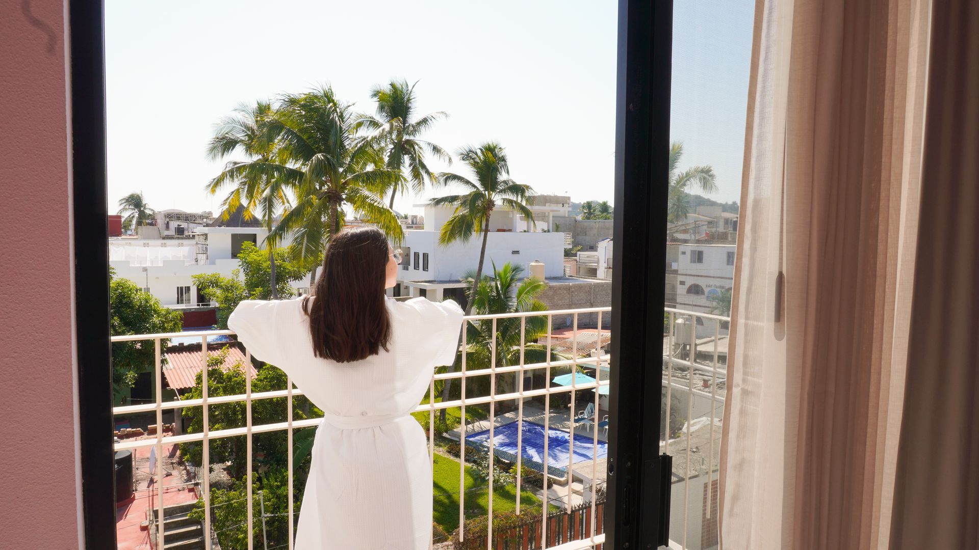 Una mujer en bata de baño está parada en un balcón mirando por la ventana.