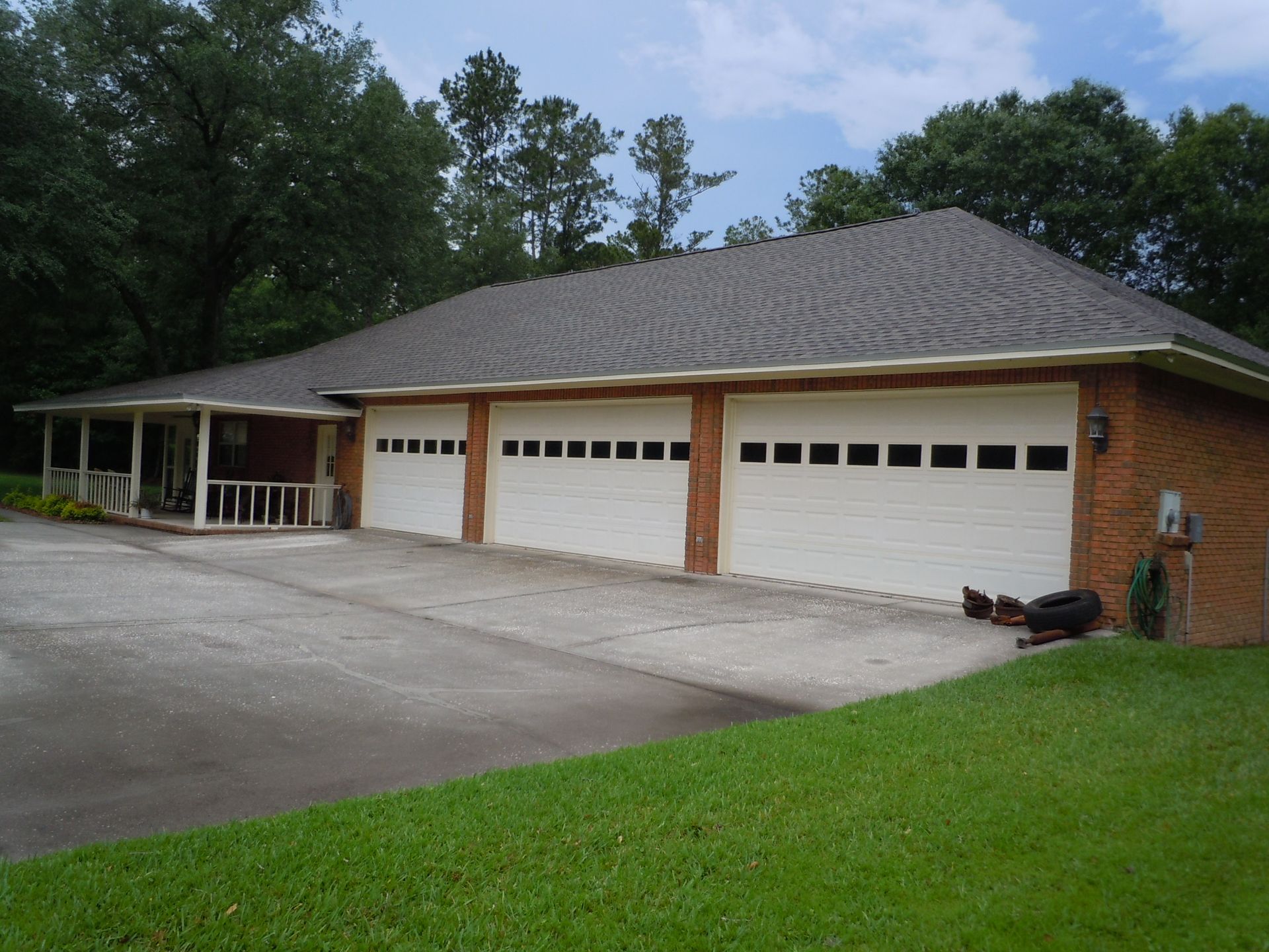 Brick house with three-car garage and a covered porch. White garage doors and a gray roof.