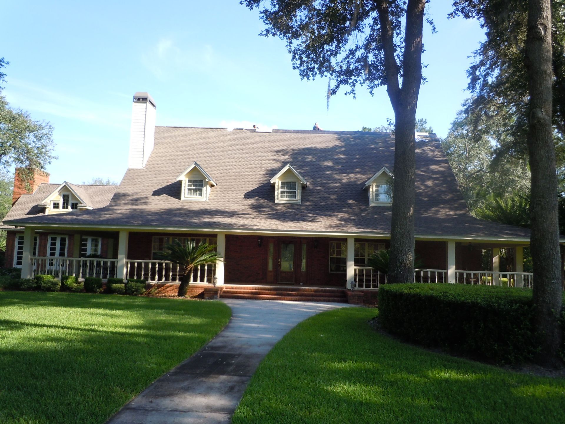 A large, red-sided house with a porch, green lawn, and walkway. Trees surround the house.