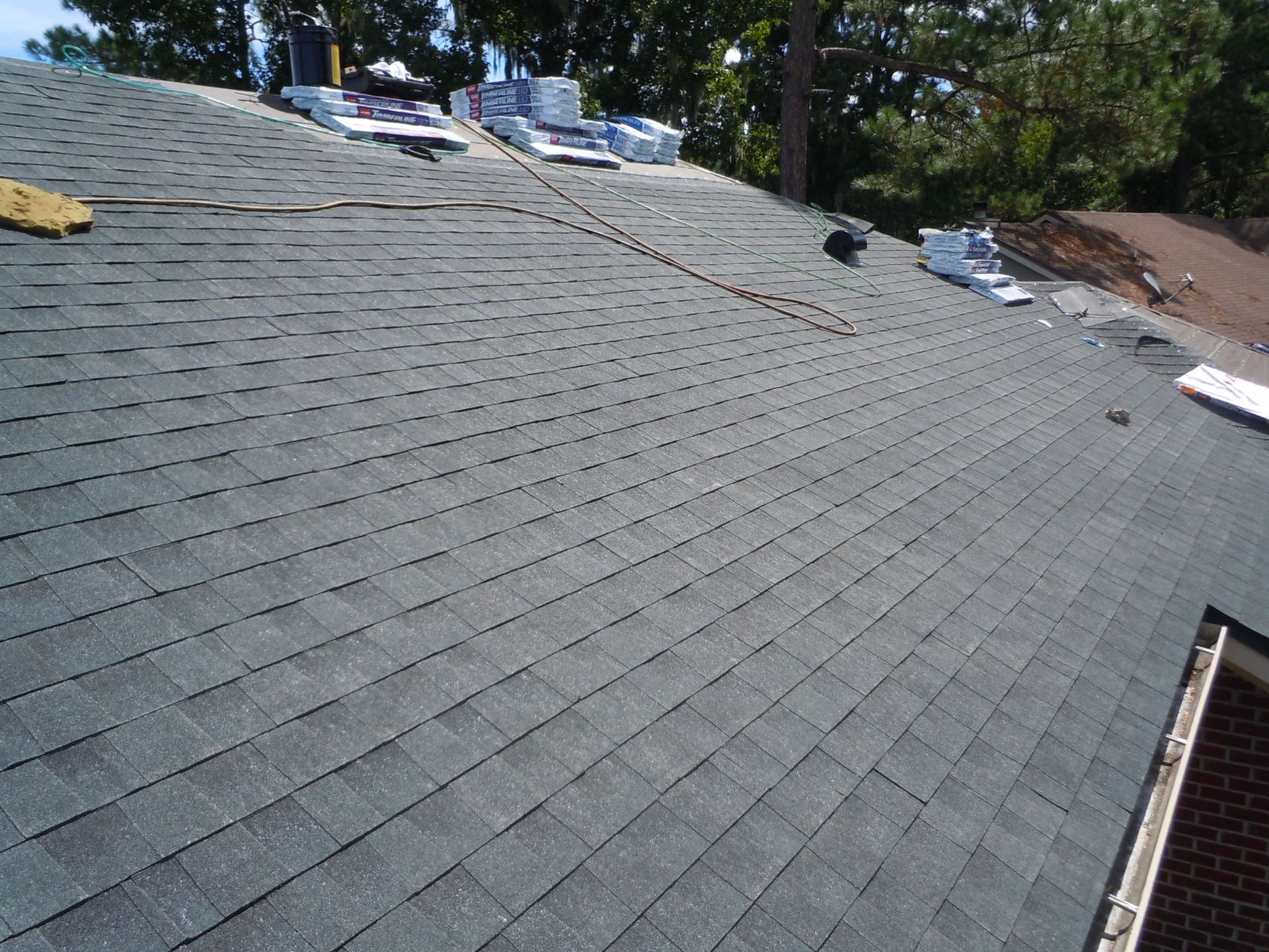Dark gray asphalt shingle roof, partially completed with materials in place, against a blue sky.