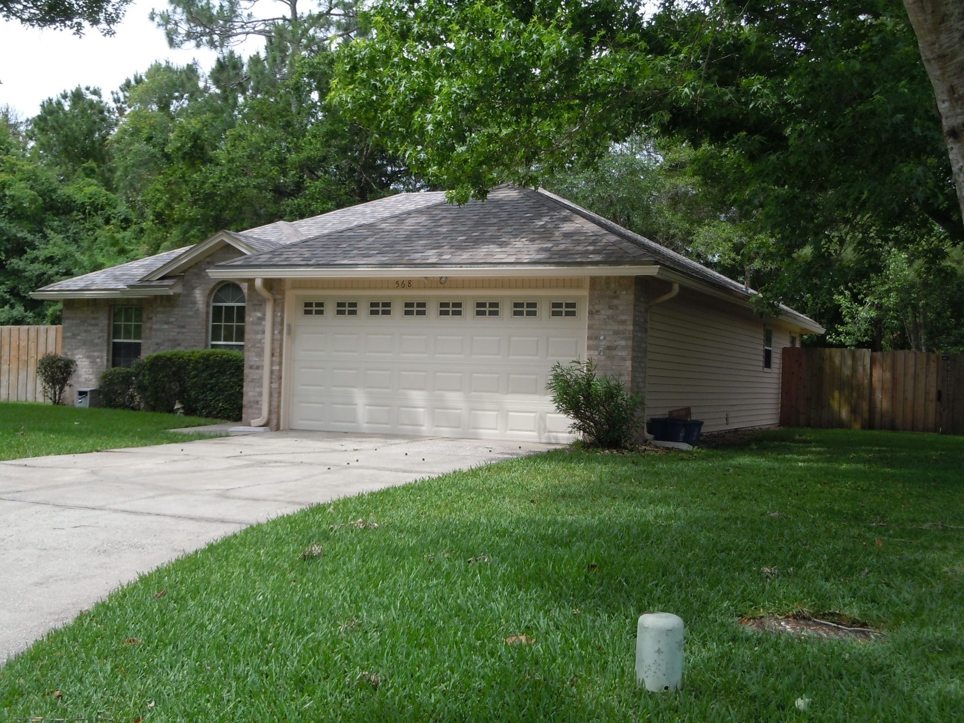 Tan brick house with a two-car garage, driveway, and green lawn.
