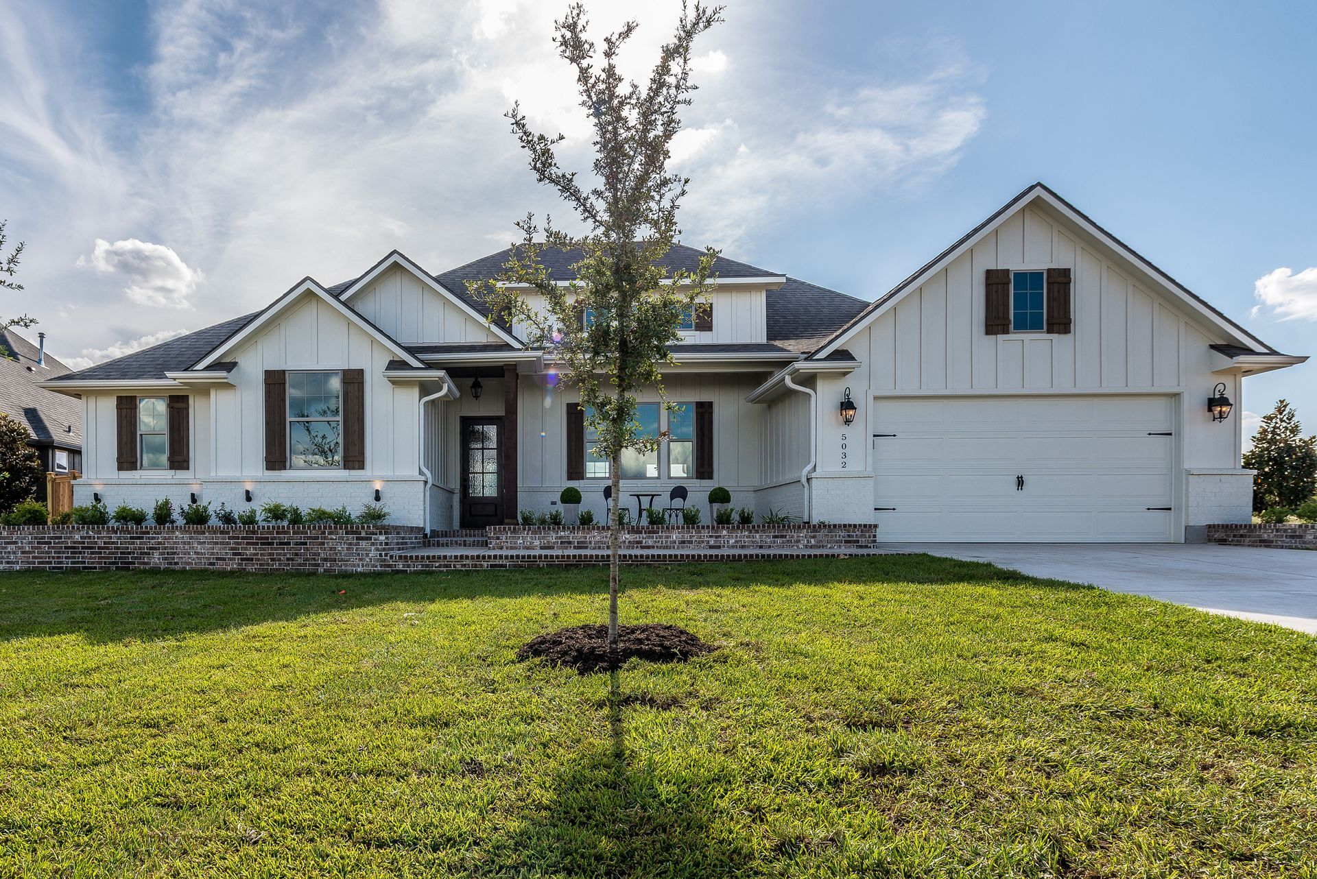 White house with brown shutters, garage, and a small tree in front.