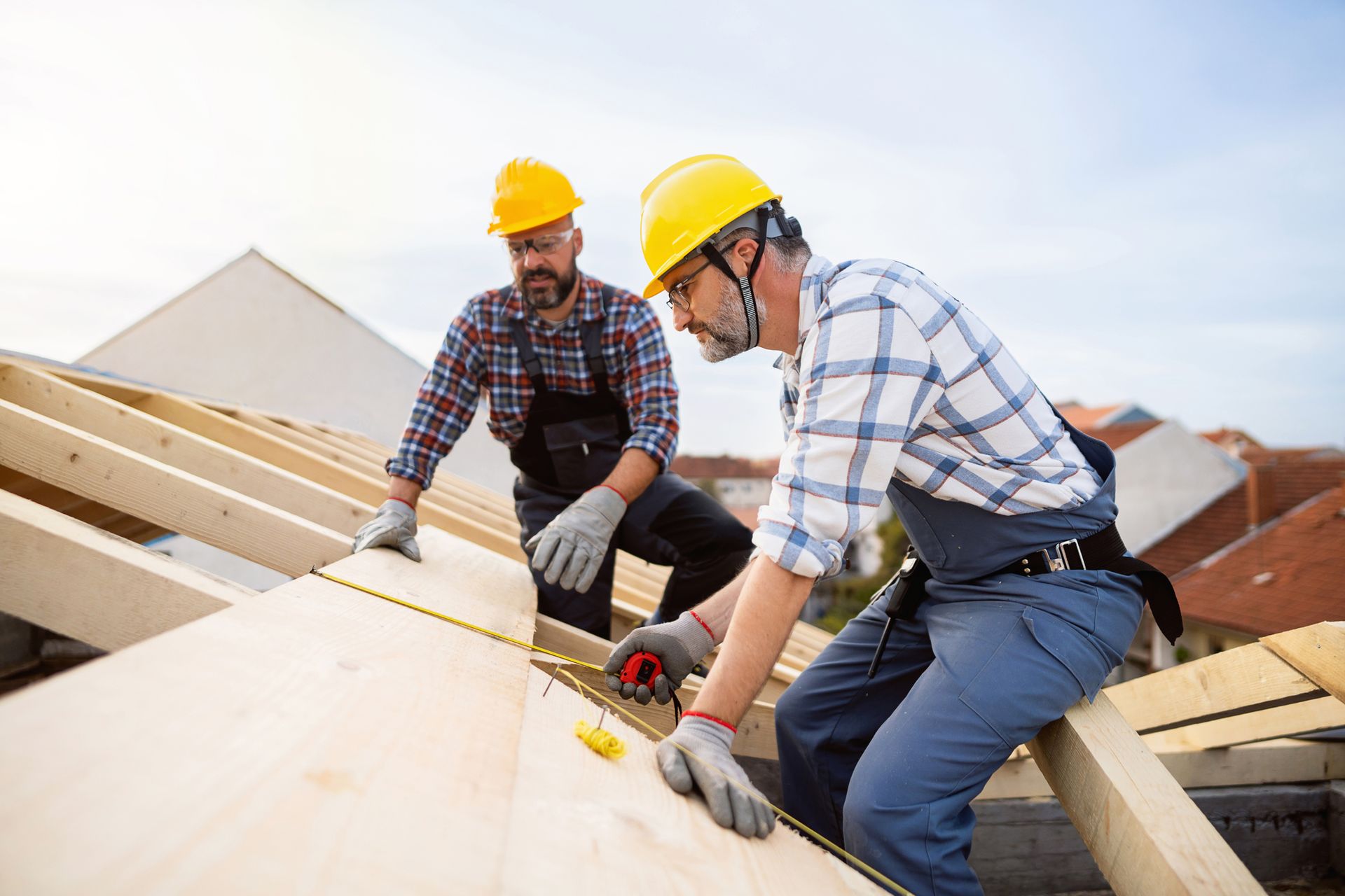 Two male roofers are repairing a roof beam while using a tape measure to measure the timbers. Two male roofers are repairing a roof beam while using a tape measure to measure the timbers.