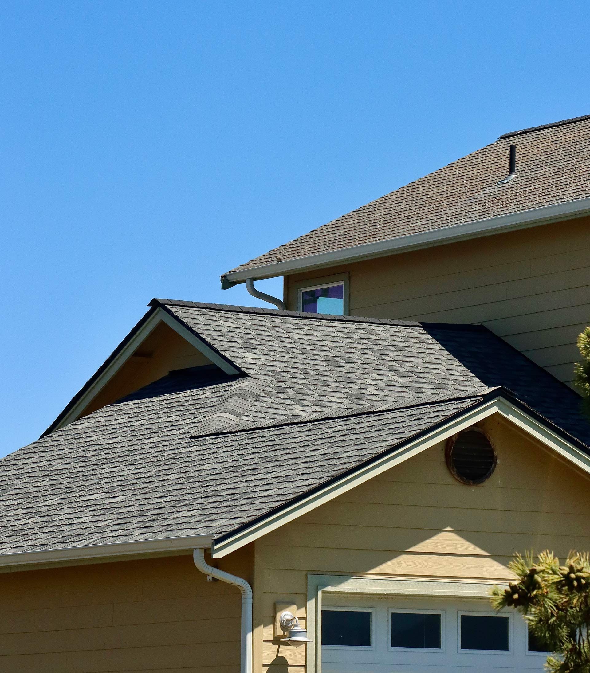Close-up of a house roof with gray asphalt shingles under a clear blue sky