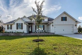 A modern white house with dark shutters, a large yard, a small tree, and a two-car garage