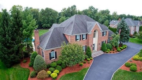 A large brick house with a grey roof, garden, and driveway in a quiet suburban area