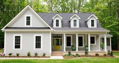A gray house with a yellow door, three dormers, and a porch with two green chairs