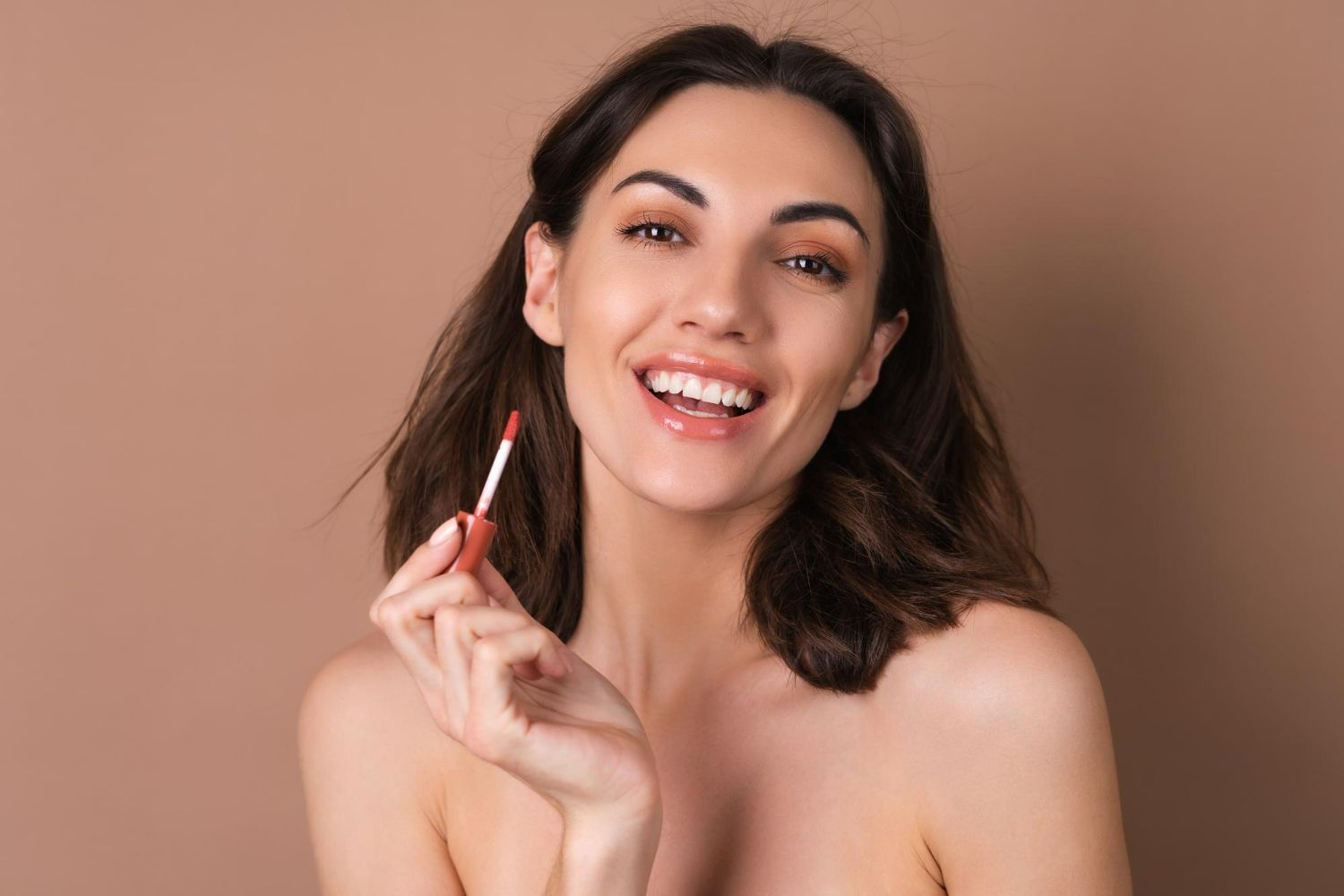 A woman is holding a lipstick in her hand and smiling.