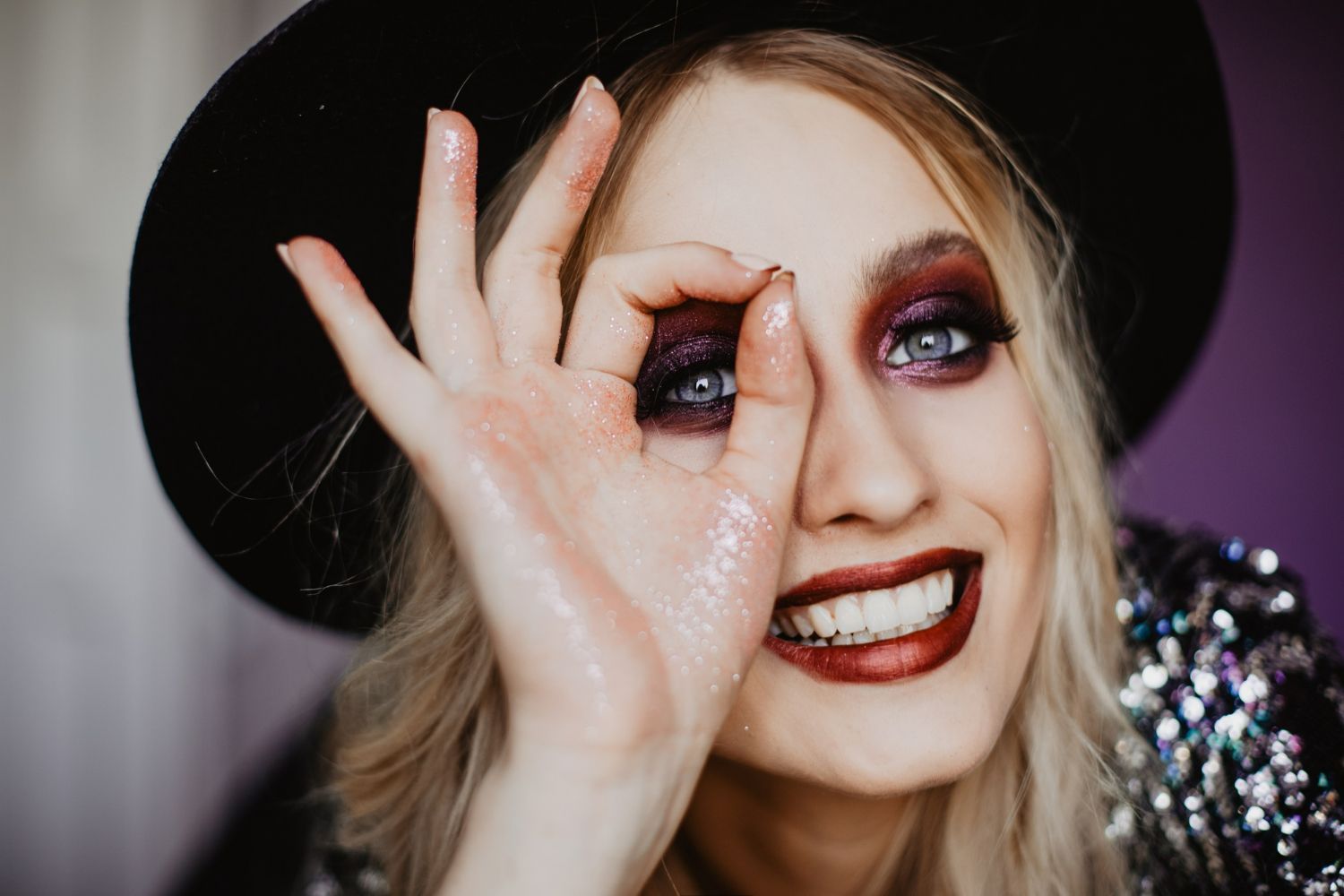 A woman wearing a black hat and red lipstick is covering her eyes with her hand.