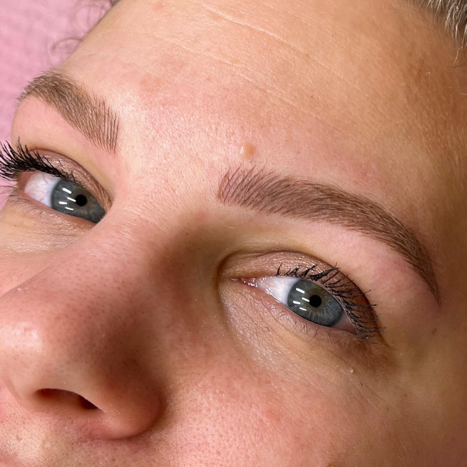 A woman is getting a permanent makeup tattoo on her eyebrows.