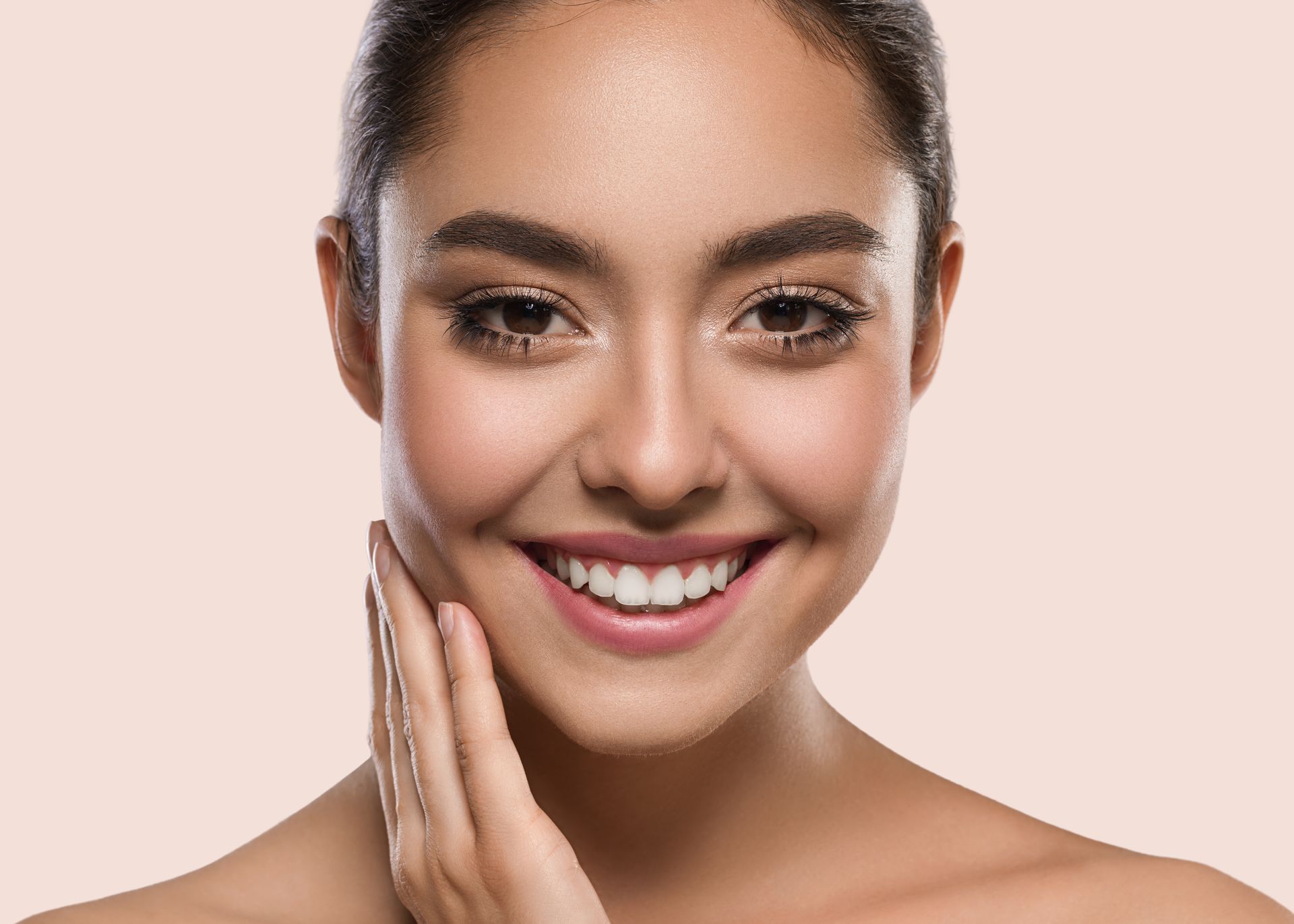 A woman is smiling and touching her face with her hand.