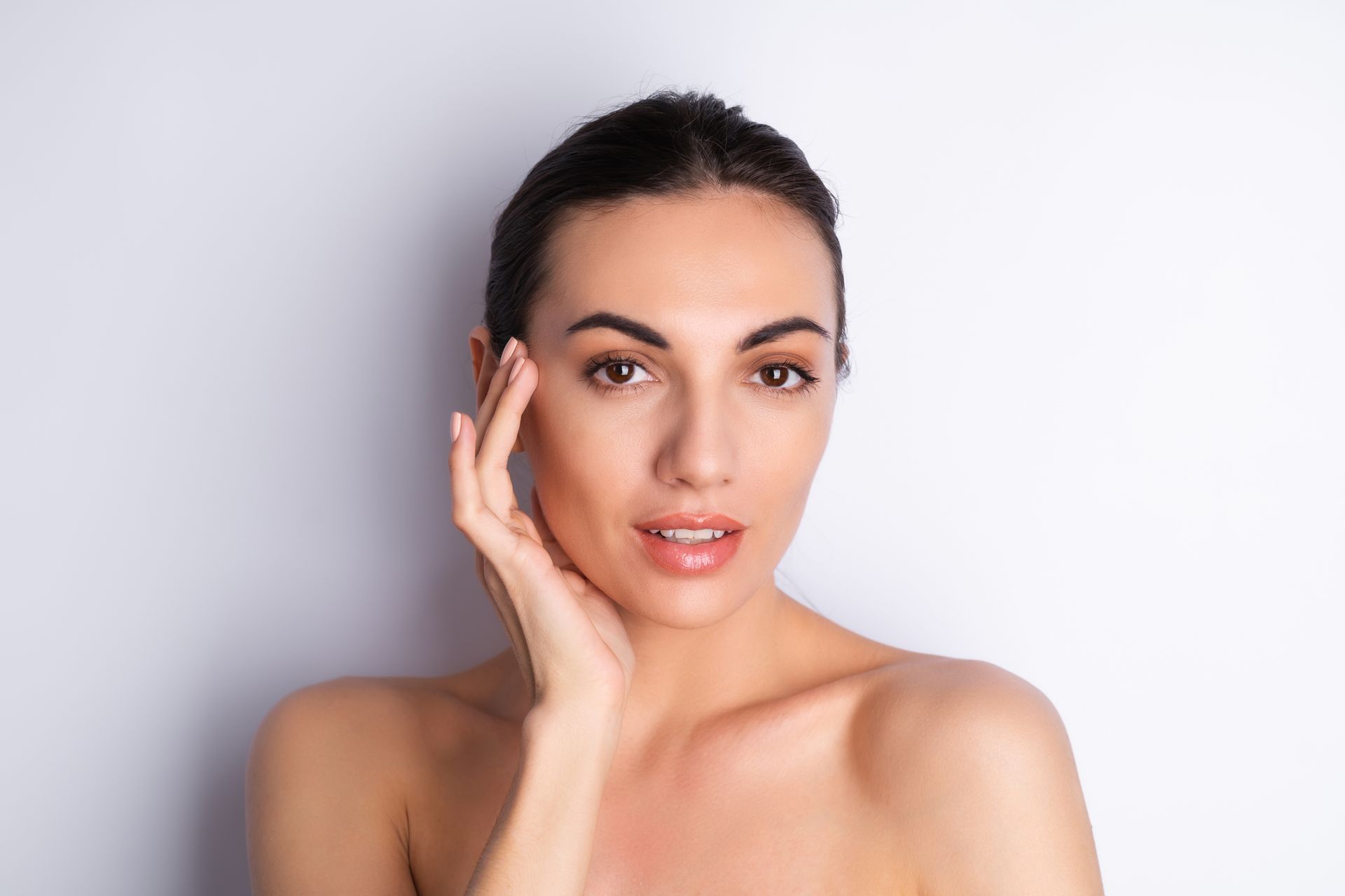 A woman is touching her face with her hand and looking at the camera.