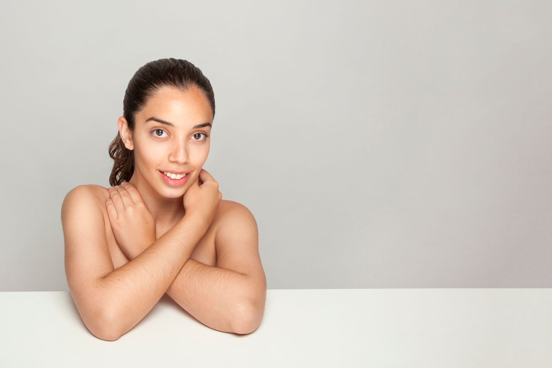 A woman without a shirt is sitting at a table with her arms crossed.