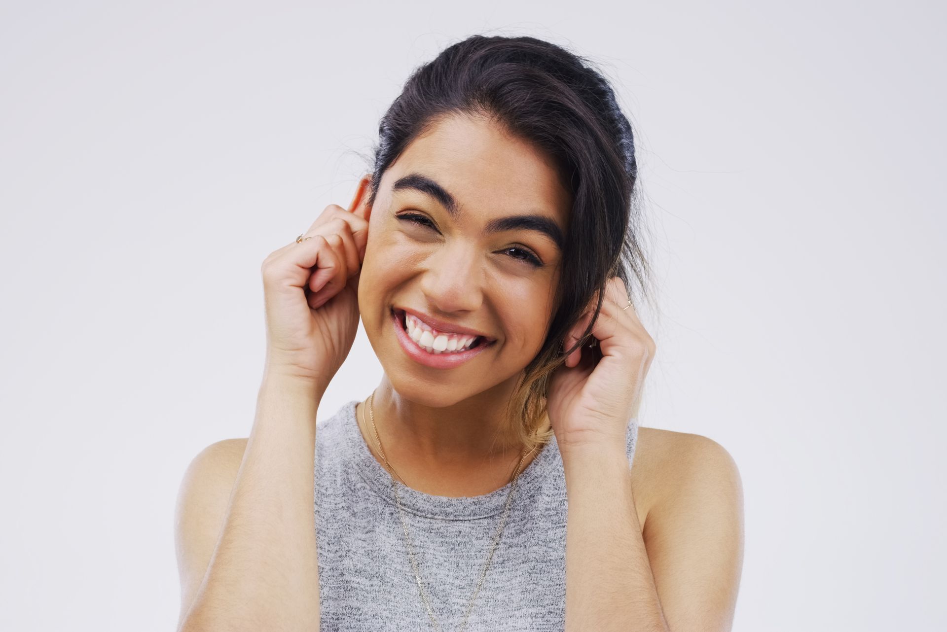 A woman is smiling and covering her ears with her hands.