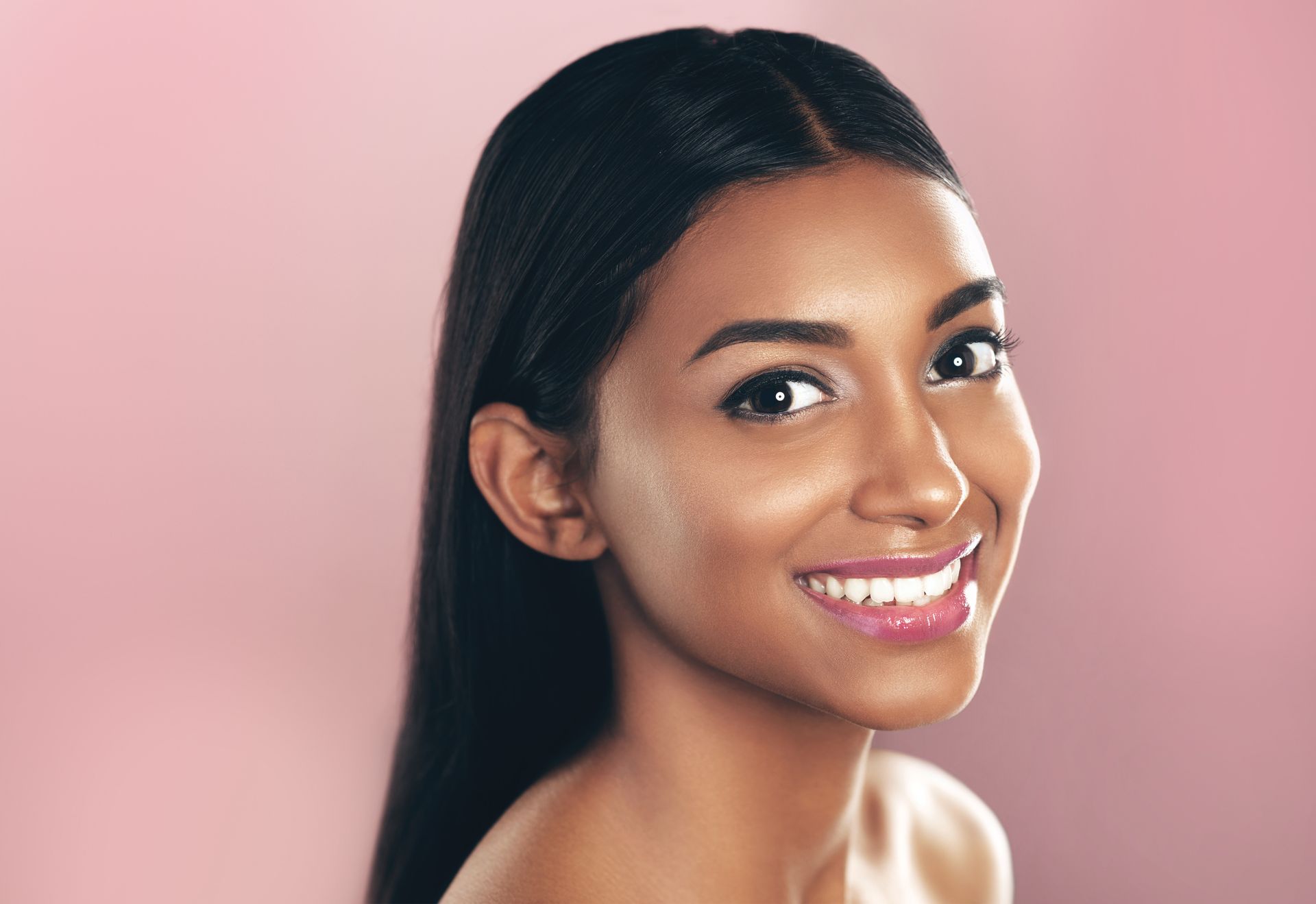 A close up of a woman 's face smiling on a pink background.