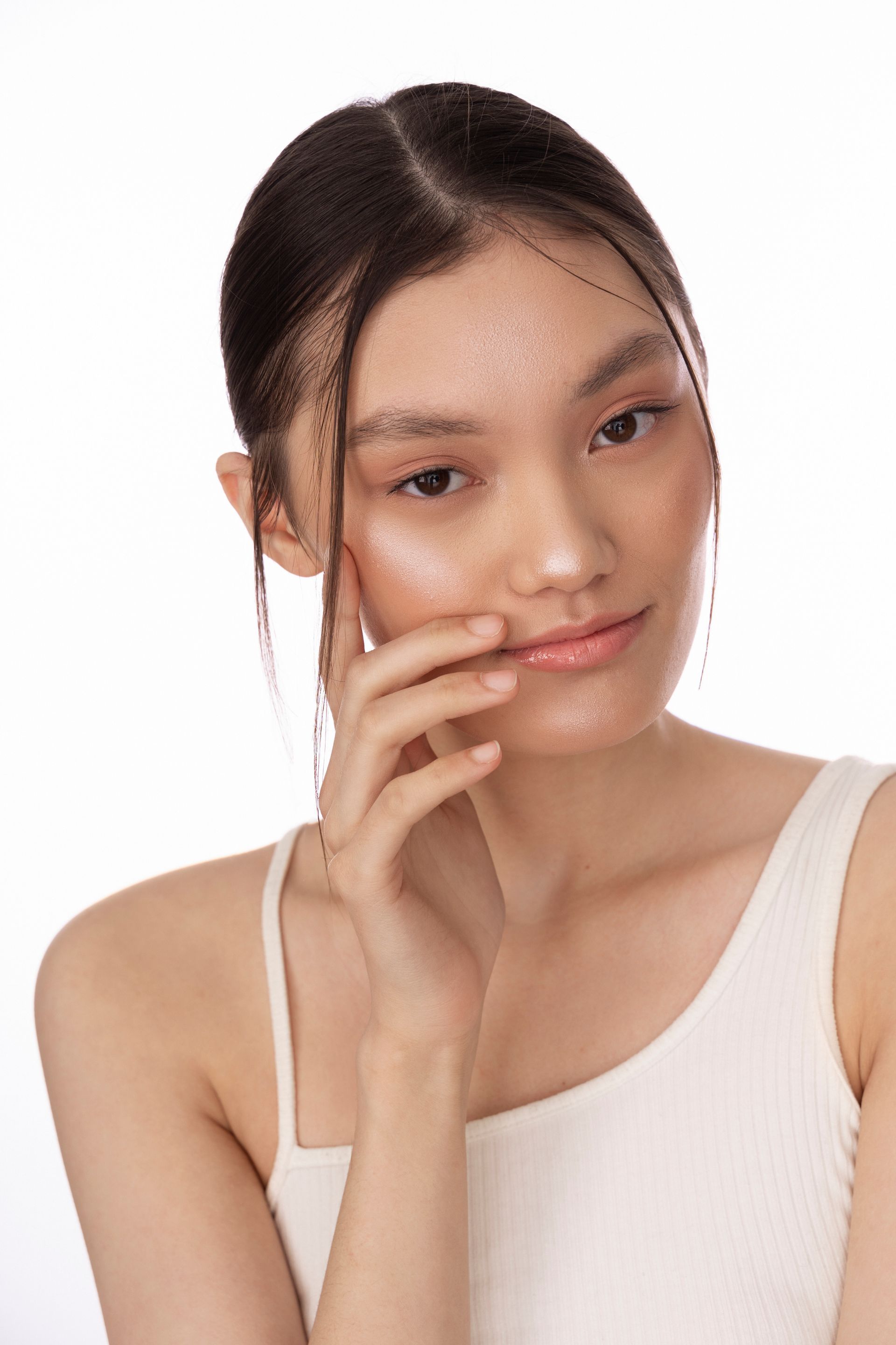 A woman in a white tank top is holding her hand to her face.