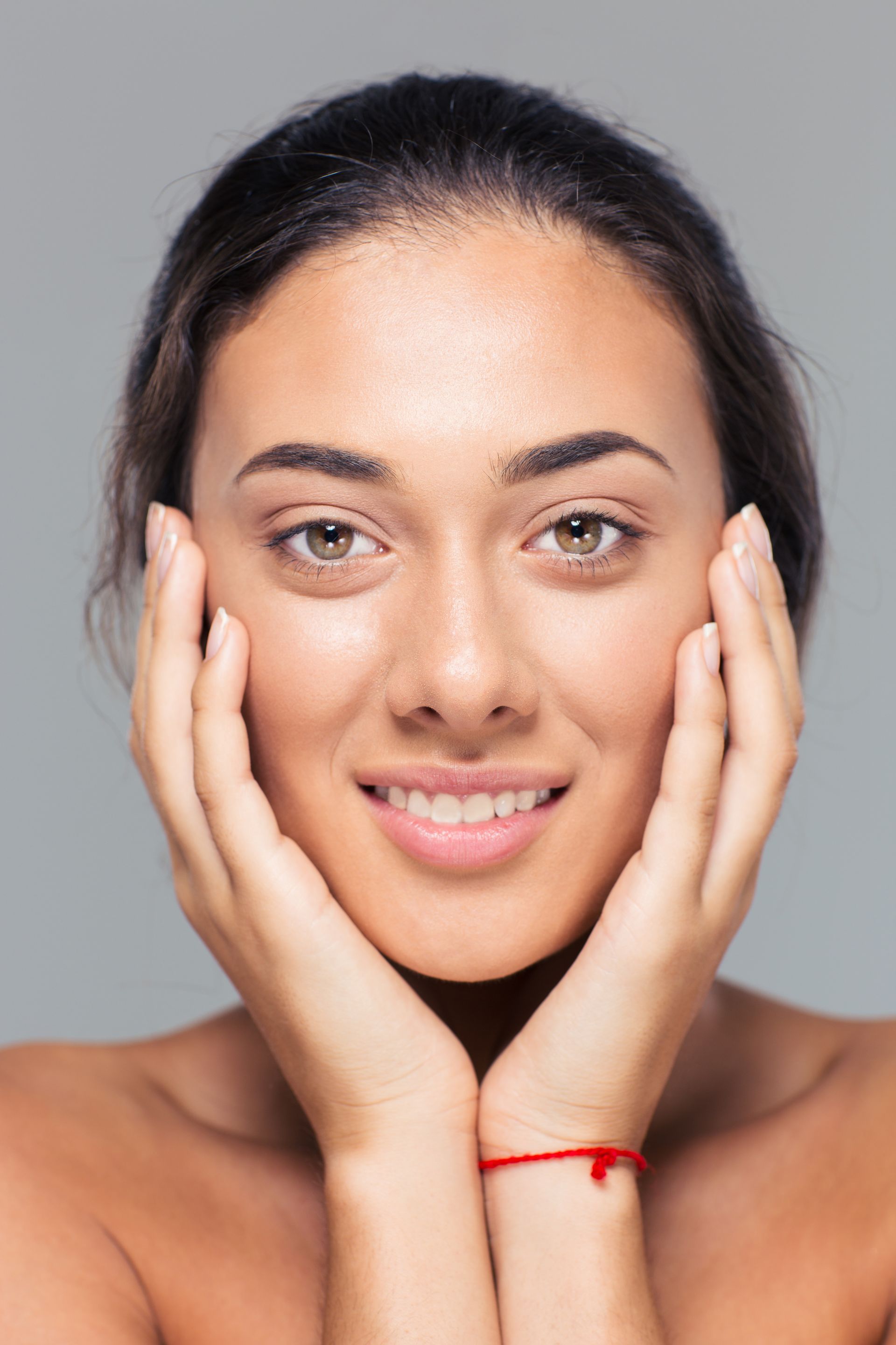 A woman is touching her face with her hands and smiling.