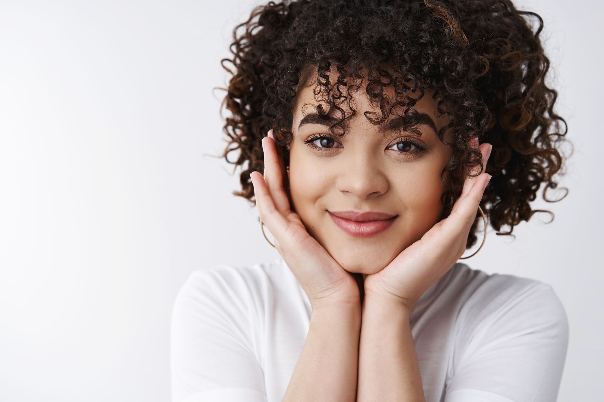 A woman with curly hair is smiling with her hands on her face.