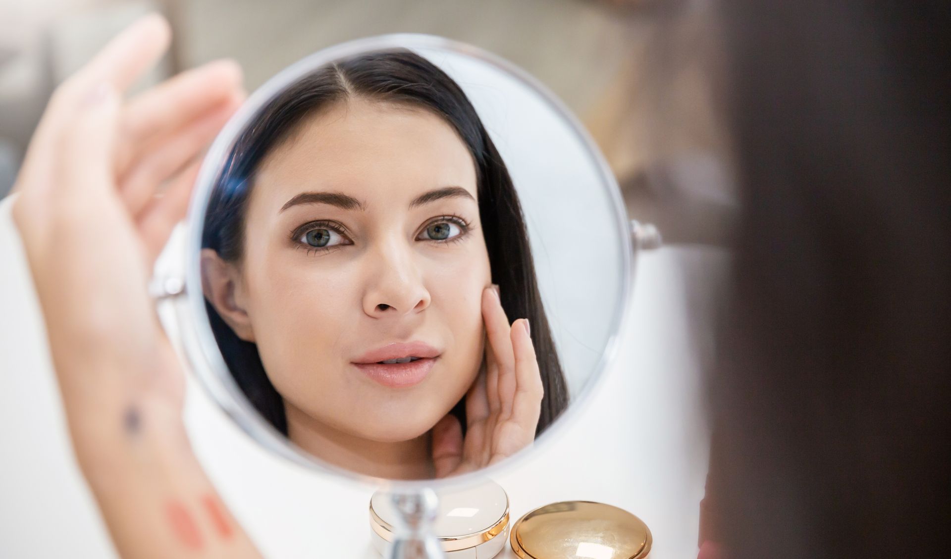 A woman is looking at her face in a mirror.