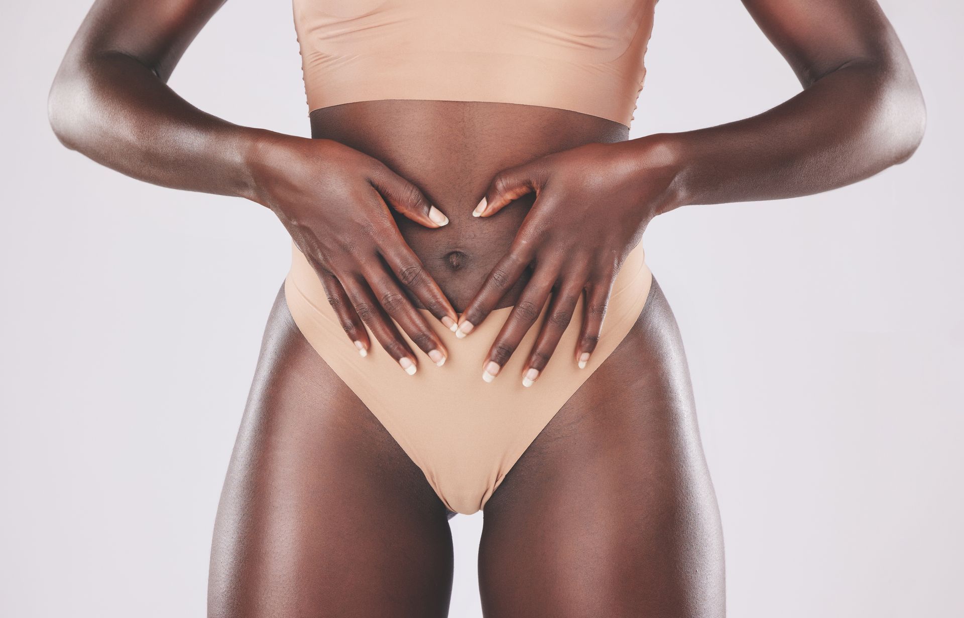 A woman is making a heart shape with her hands on her stomach.