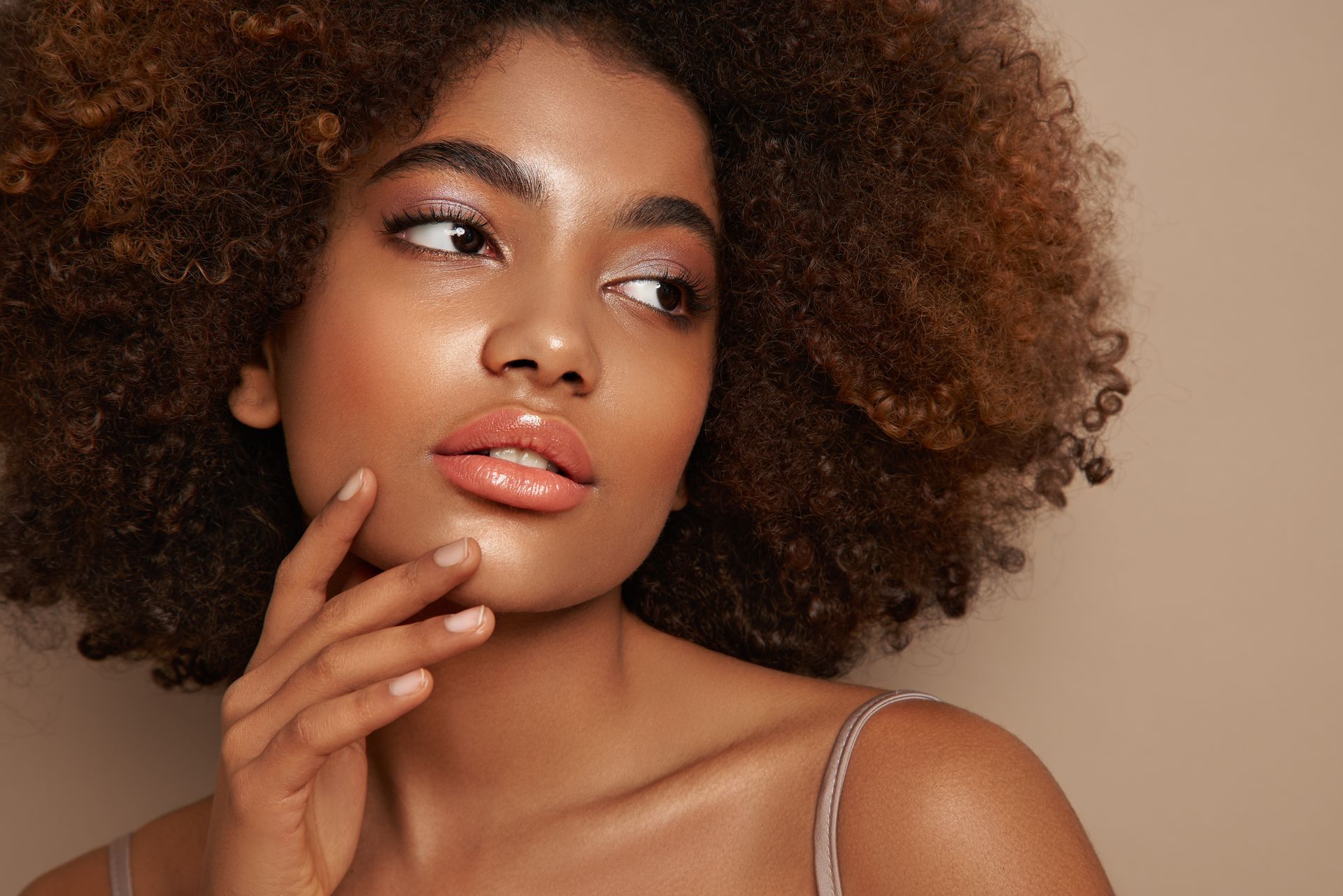 A woman with curly hair is touching her face with her hand.