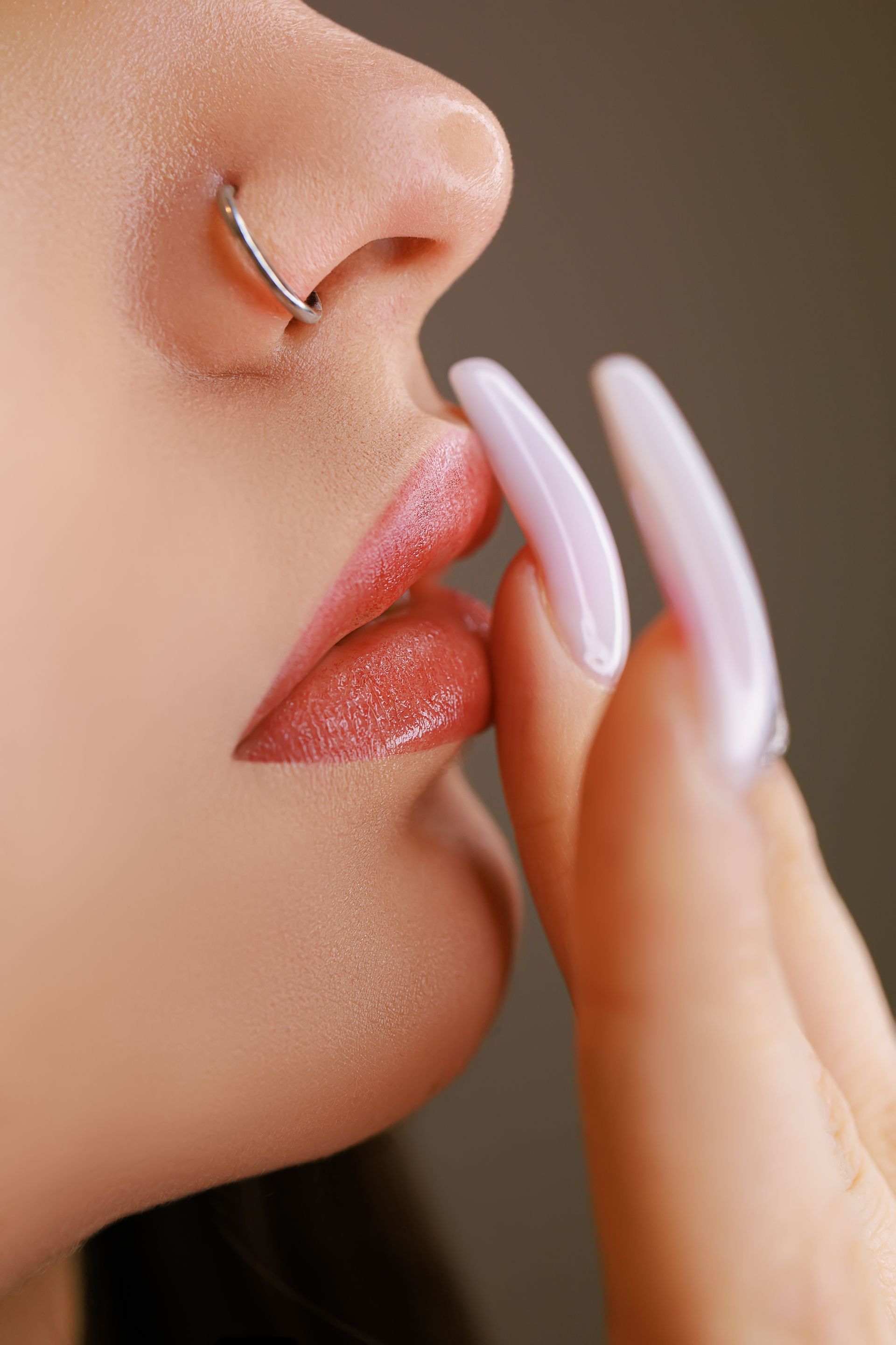 A close up of a woman 's face with a nose ring and long nails.