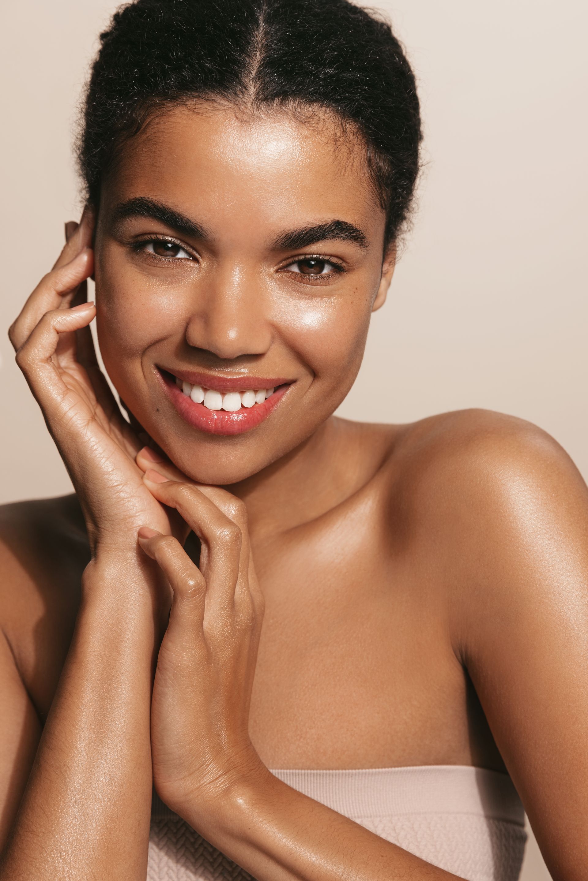 A woman is smiling and touching her face with her hands.