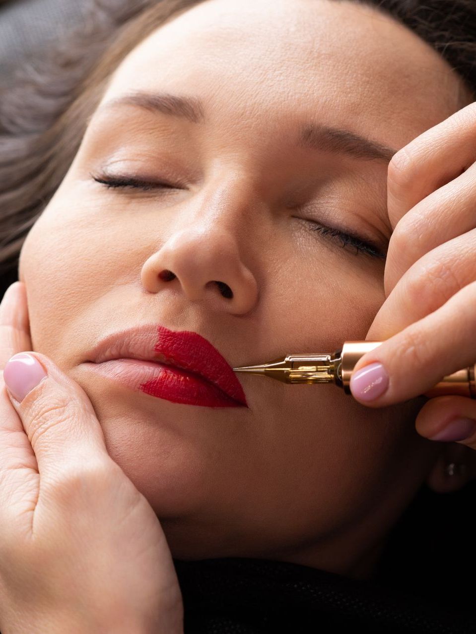 A woman is getting her lips painted with red lipstick.