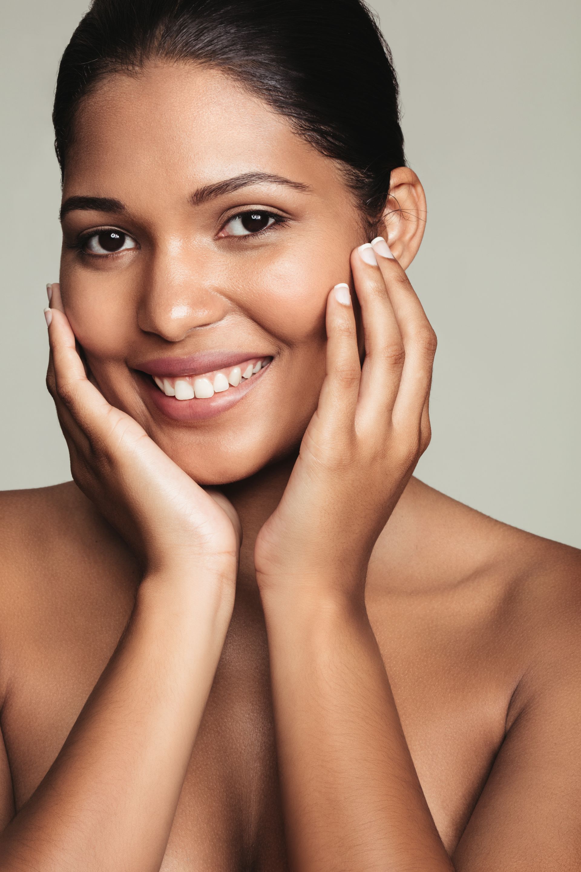 A woman is smiling and touching her face with her hands.