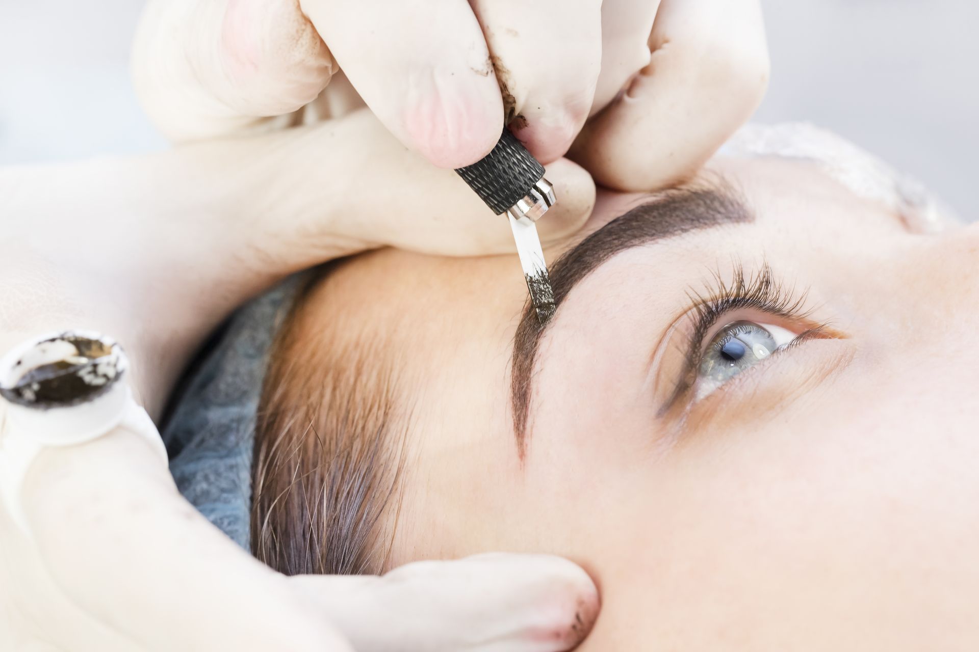 A woman is getting her eyebrows painted by a tattoo artist.