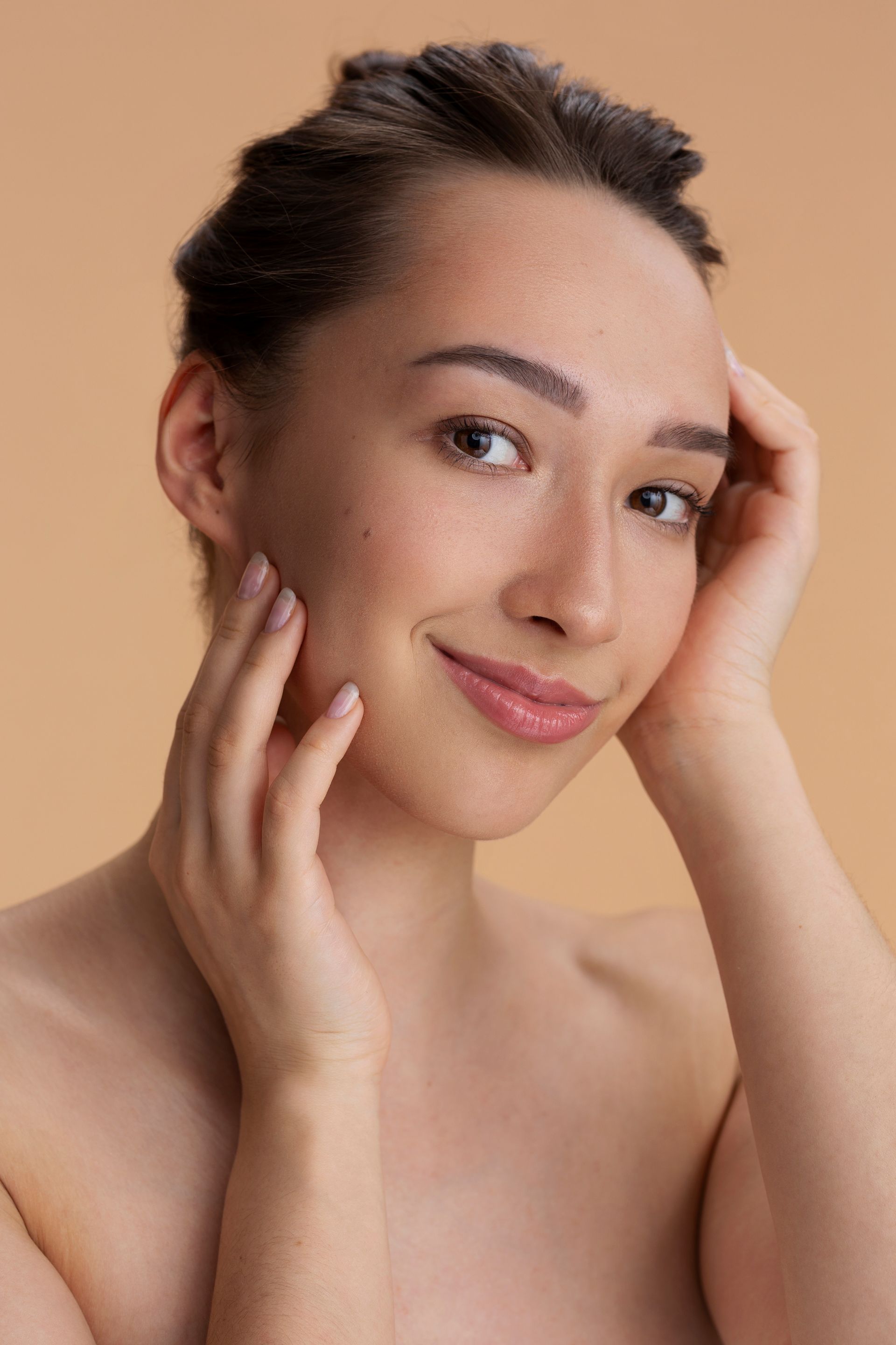 A woman is touching her face with her hands and smiling.