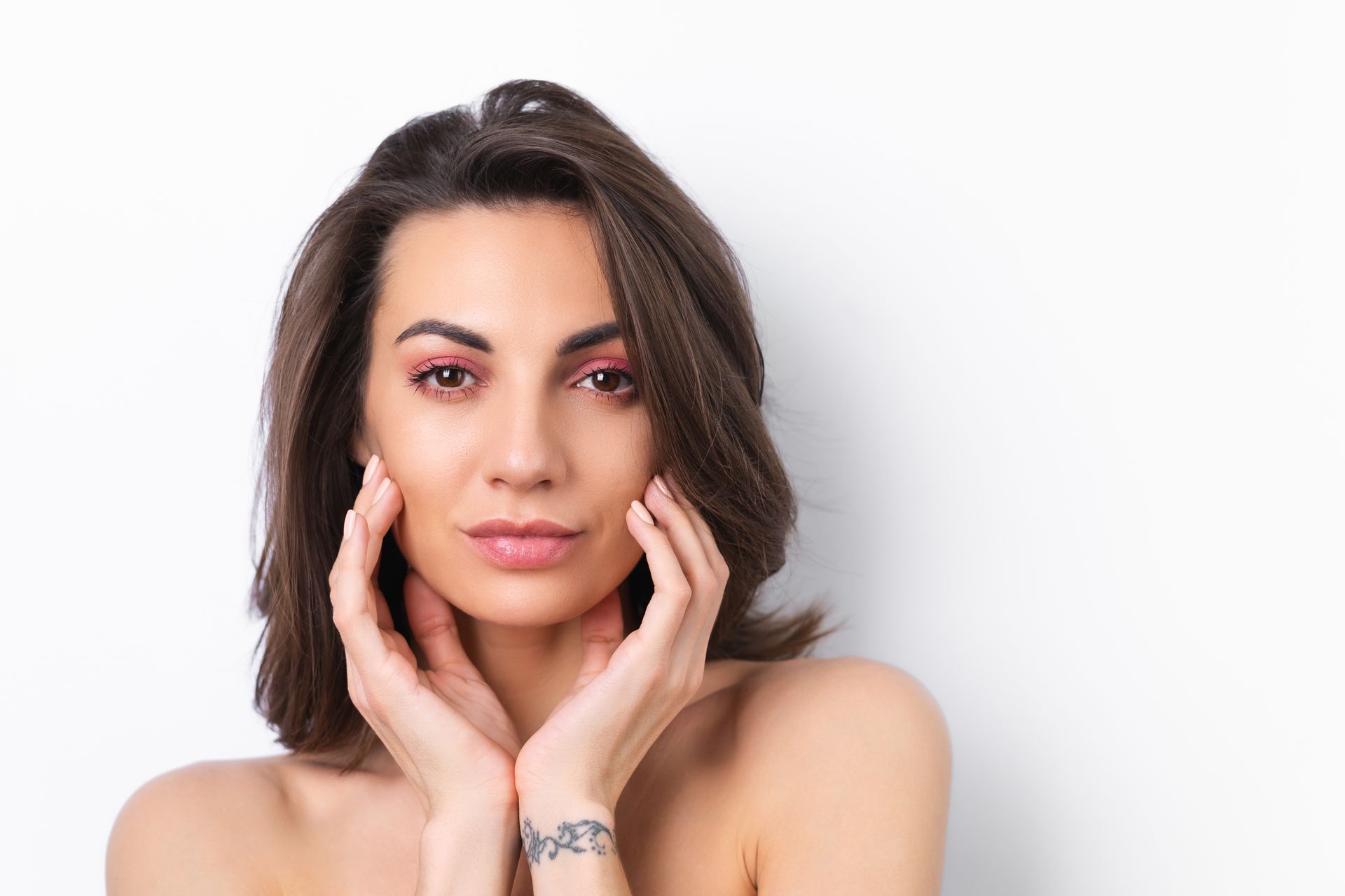 A woman with a tattoo on her wrist is touching her face.